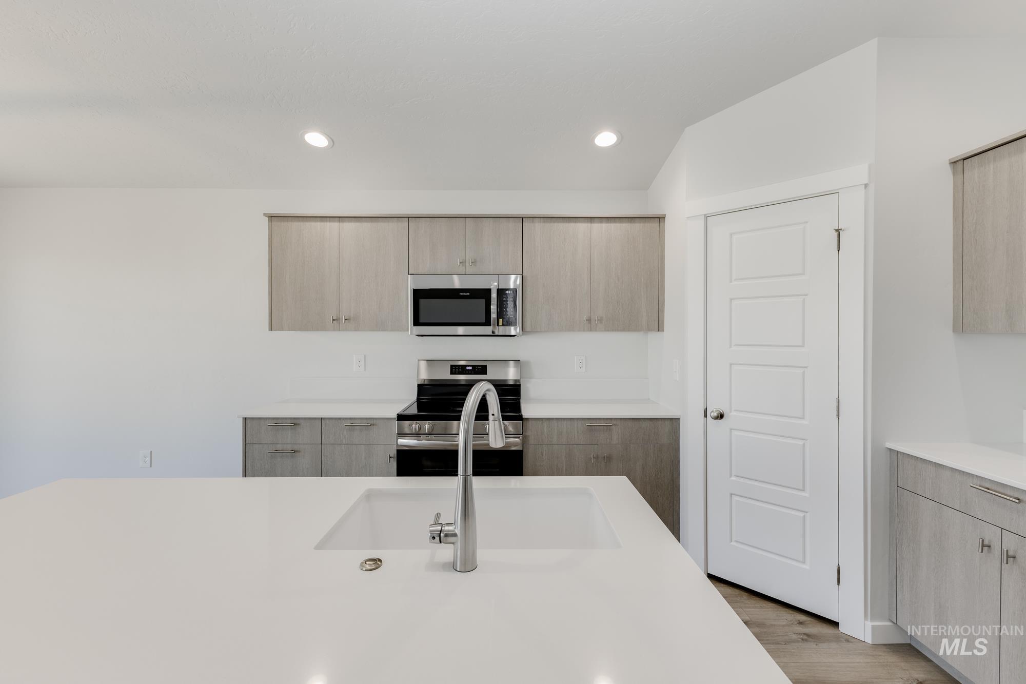 Kitchen featuring modern cabinets, stainless steel appliances, light brown cabinetry, and recessed lighting