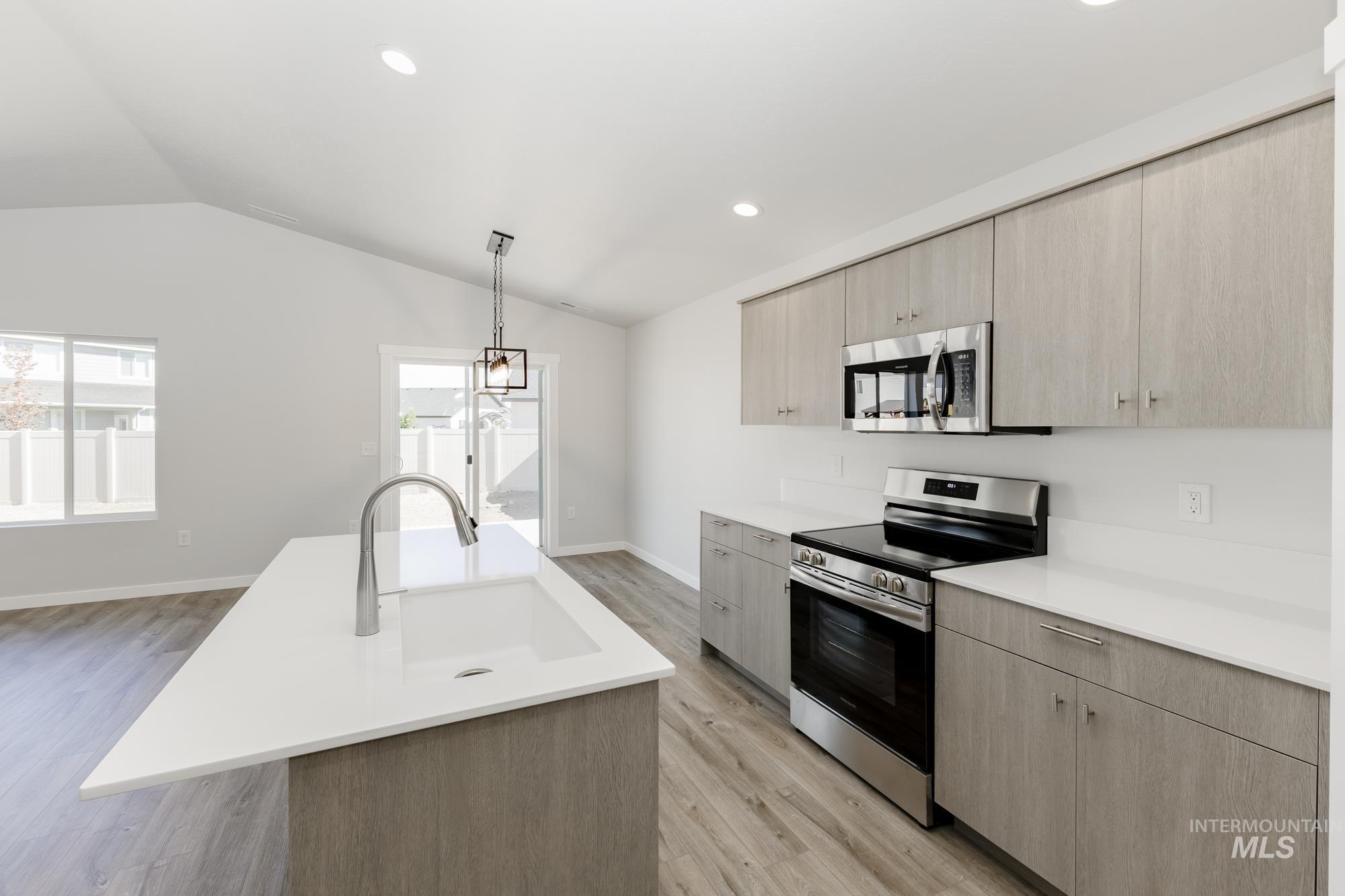 Kitchen featuring stainless steel appliances, light brown cabinetry, pendant lighting, lofted ceiling, and modern cabinets