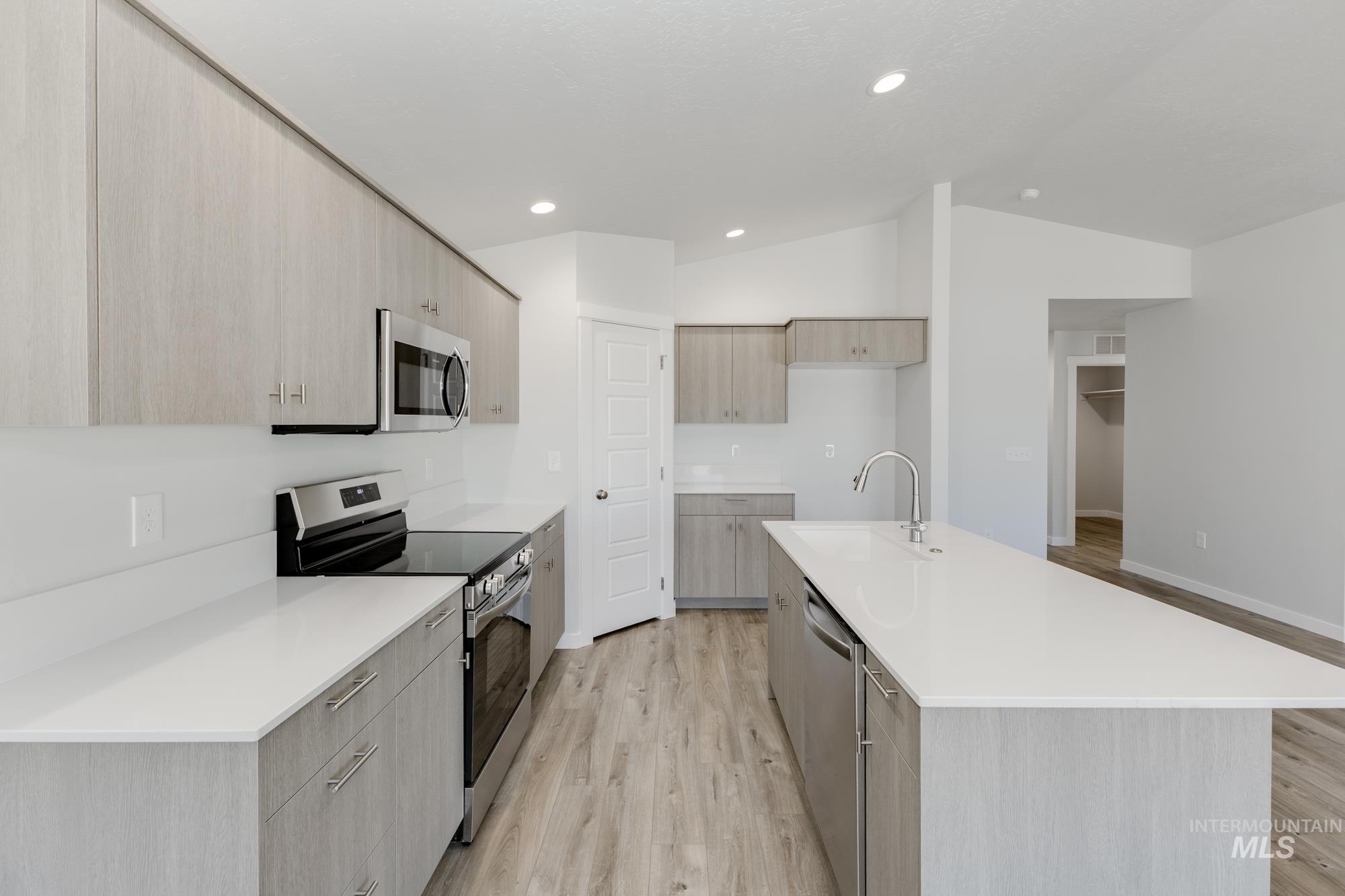 Kitchen featuring stainless steel appliances, light wood-type flooring, modern cabinets, light brown cabinetry, and lofted ceiling