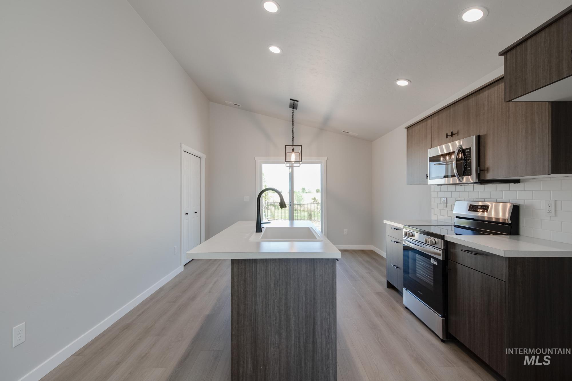 Kitchen featuring modern cabinets, stainless steel appliances, light countertops, backsplash, and lofted ceiling