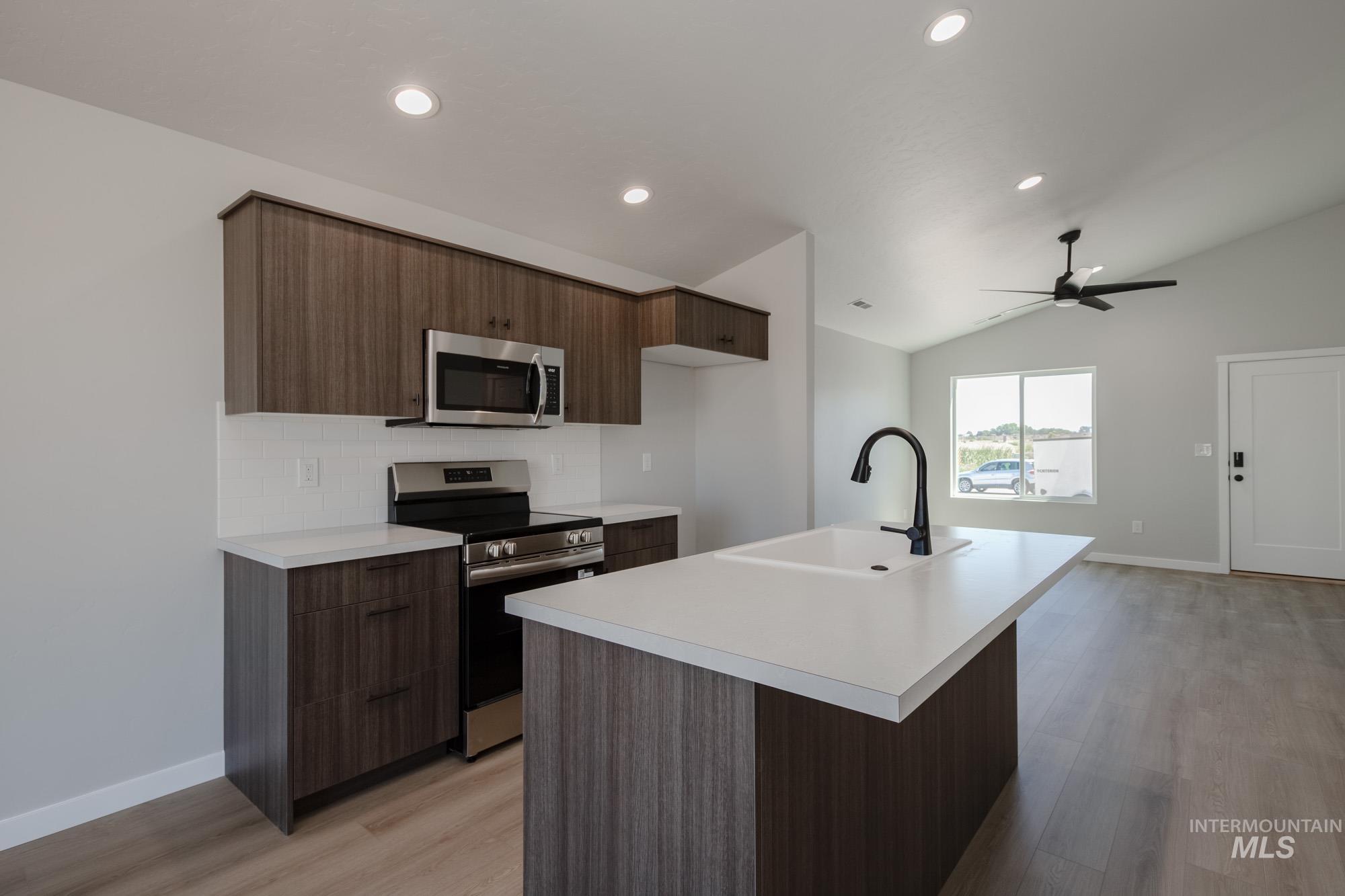Kitchen featuring stainless steel appliances, modern cabinets, light countertops, vaulted ceiling, and a center island with sink