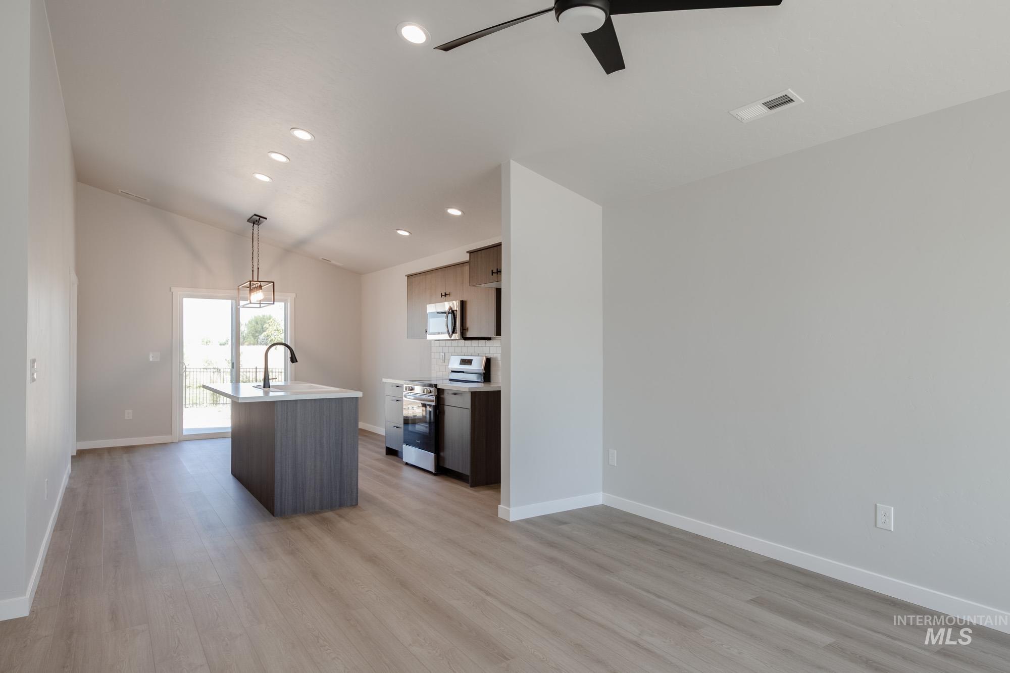Kitchen featuring an island with sink, decorative backsplash, stainless steel appliances, light wood-style flooring, and vaulted ceiling