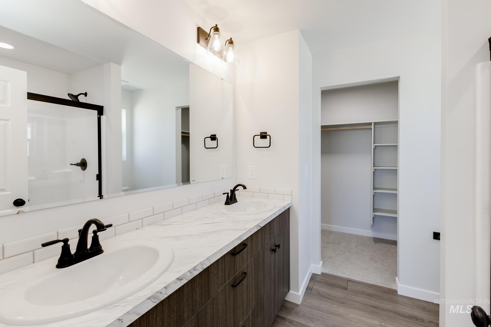 Bathroom with a walk in closet, light wood finished floors, double vanity, and a stall shower
