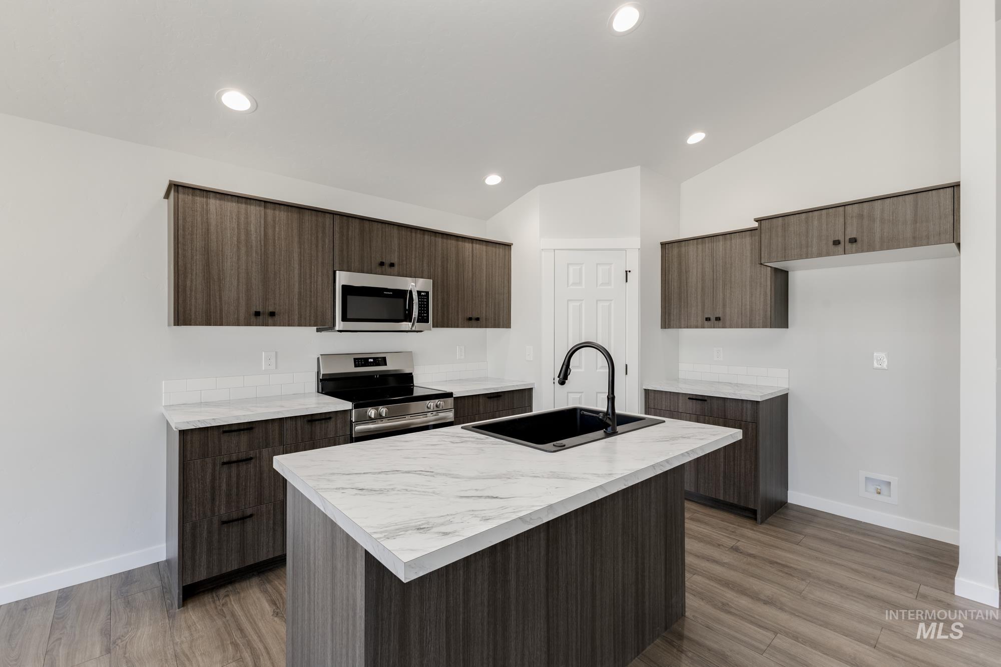 Kitchen featuring light countertops, stainless steel appliances, light wood finished floors, a kitchen island with sink, and vaulted ceiling