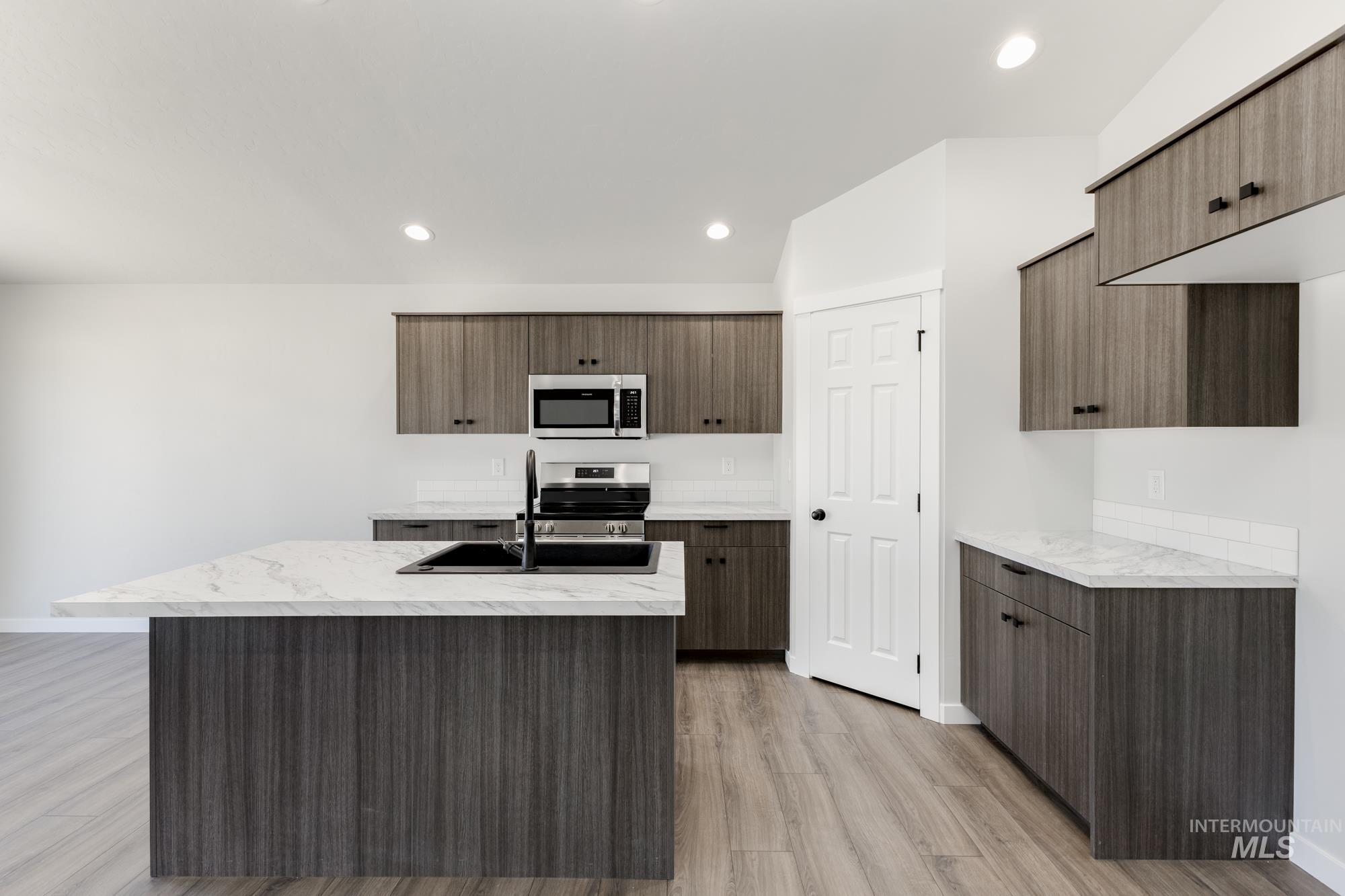 Kitchen with light wood-style flooring, a center island with sink, appliances with stainless steel finishes, recessed lighting, and modern cabinets