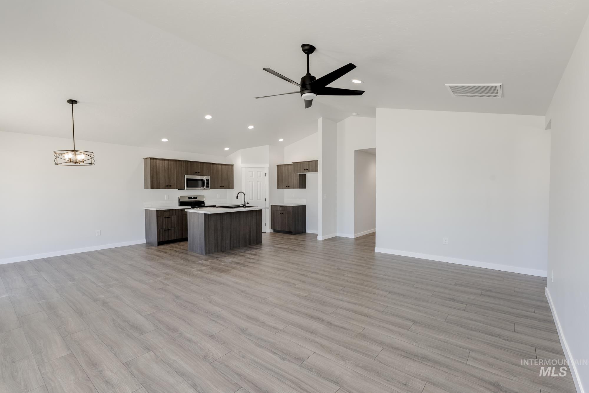 Unfurnished living room featuring light wood-style flooring, ceiling fan, recessed lighting, high vaulted ceiling, and a chandelier