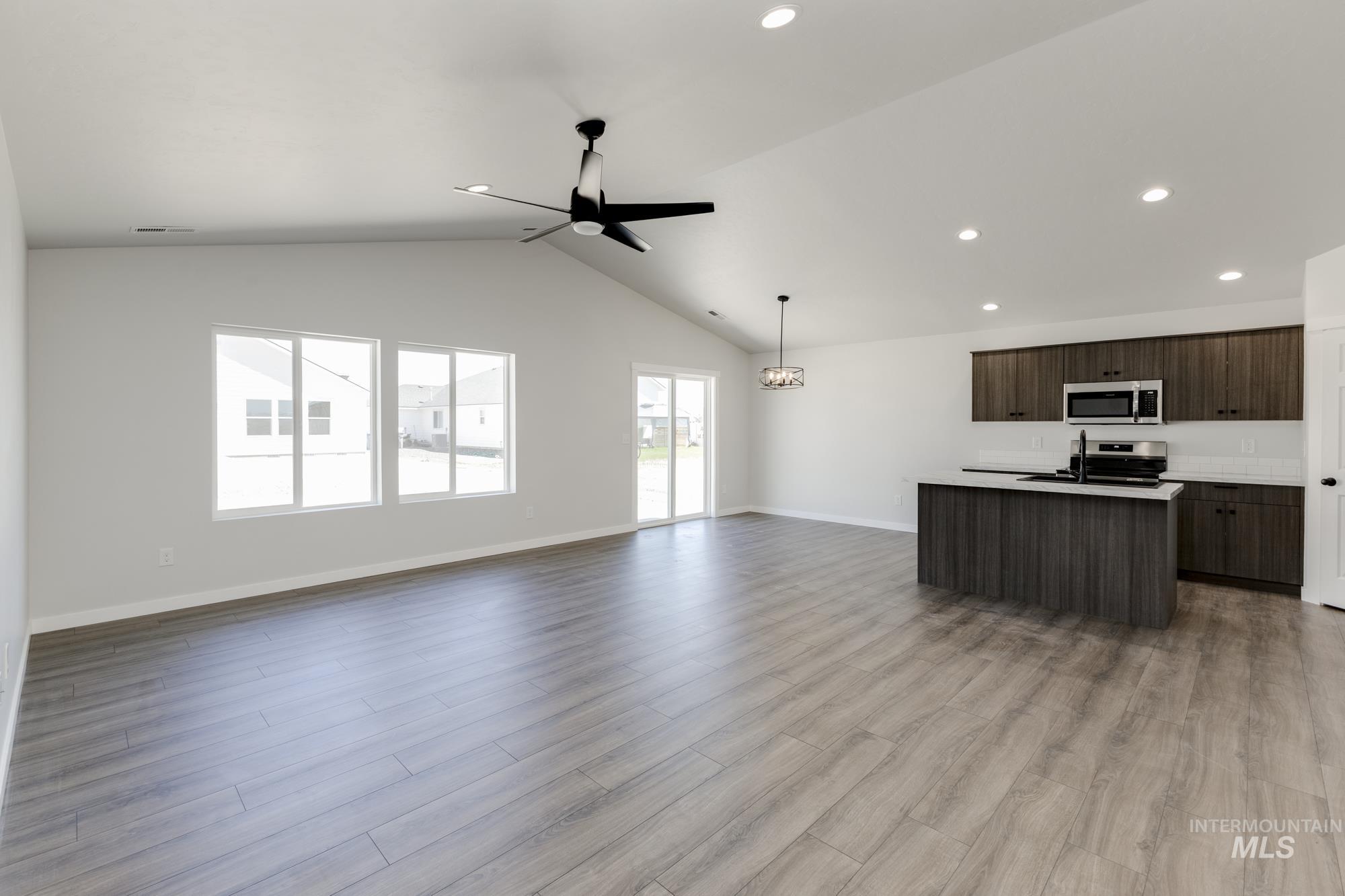 Kitchen with open floor plan, a center island with sink, dark brown cabinetry, lofted ceiling, and light wood finished floors