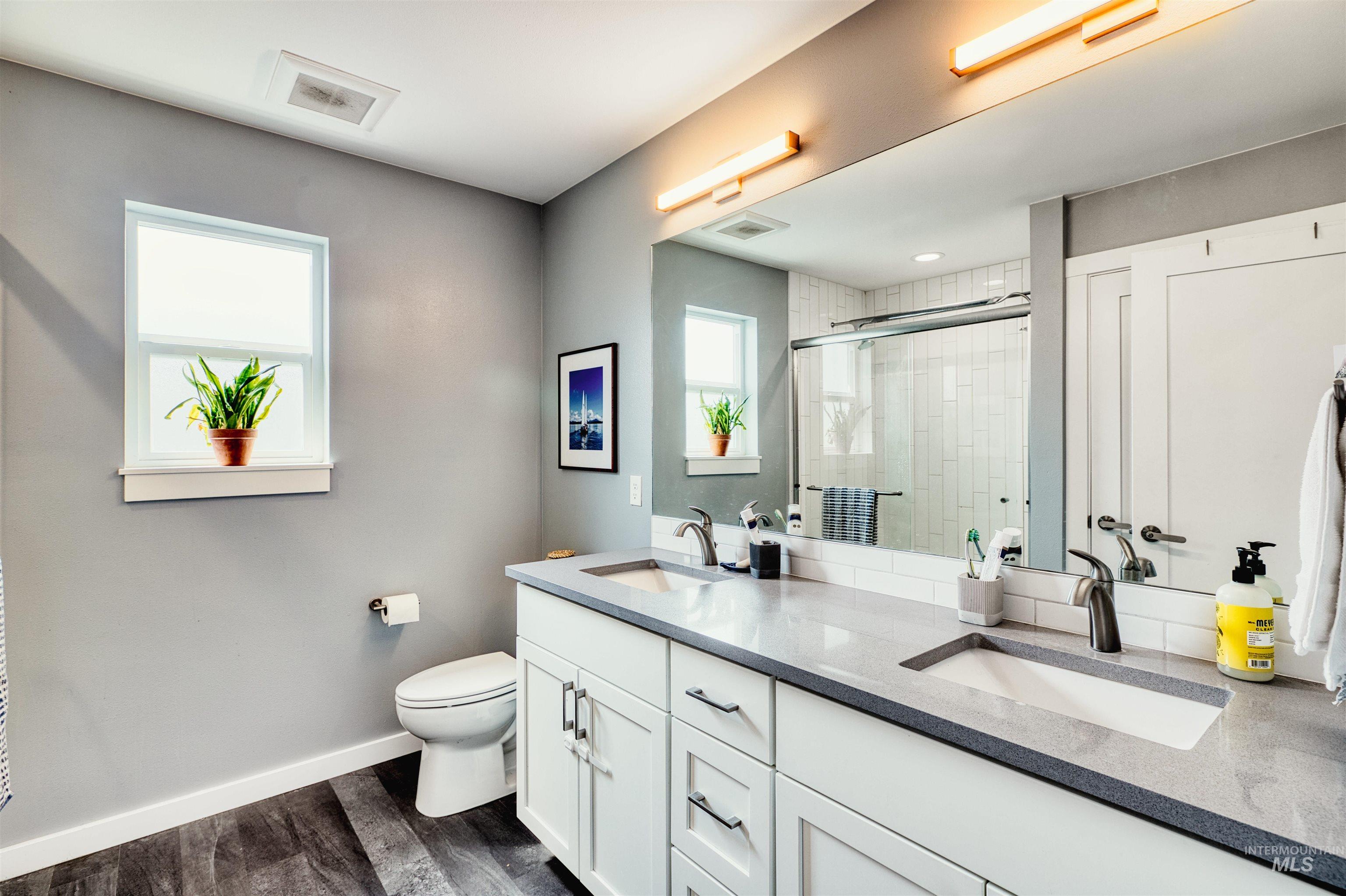 Full bath with a shower stall, double vanity, and dark wood-style floors