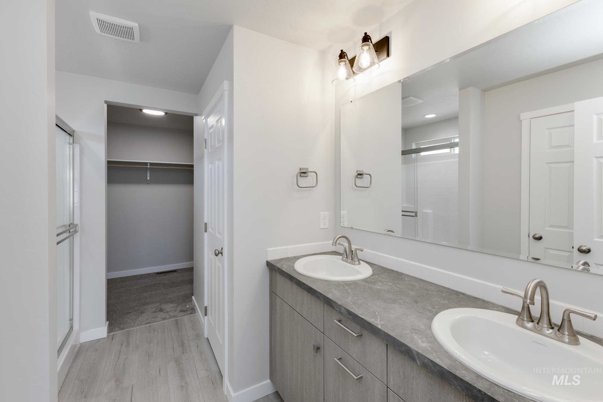 Full bathroom with a shower stall, double vanity, light wood-style floors, and a spacious closet