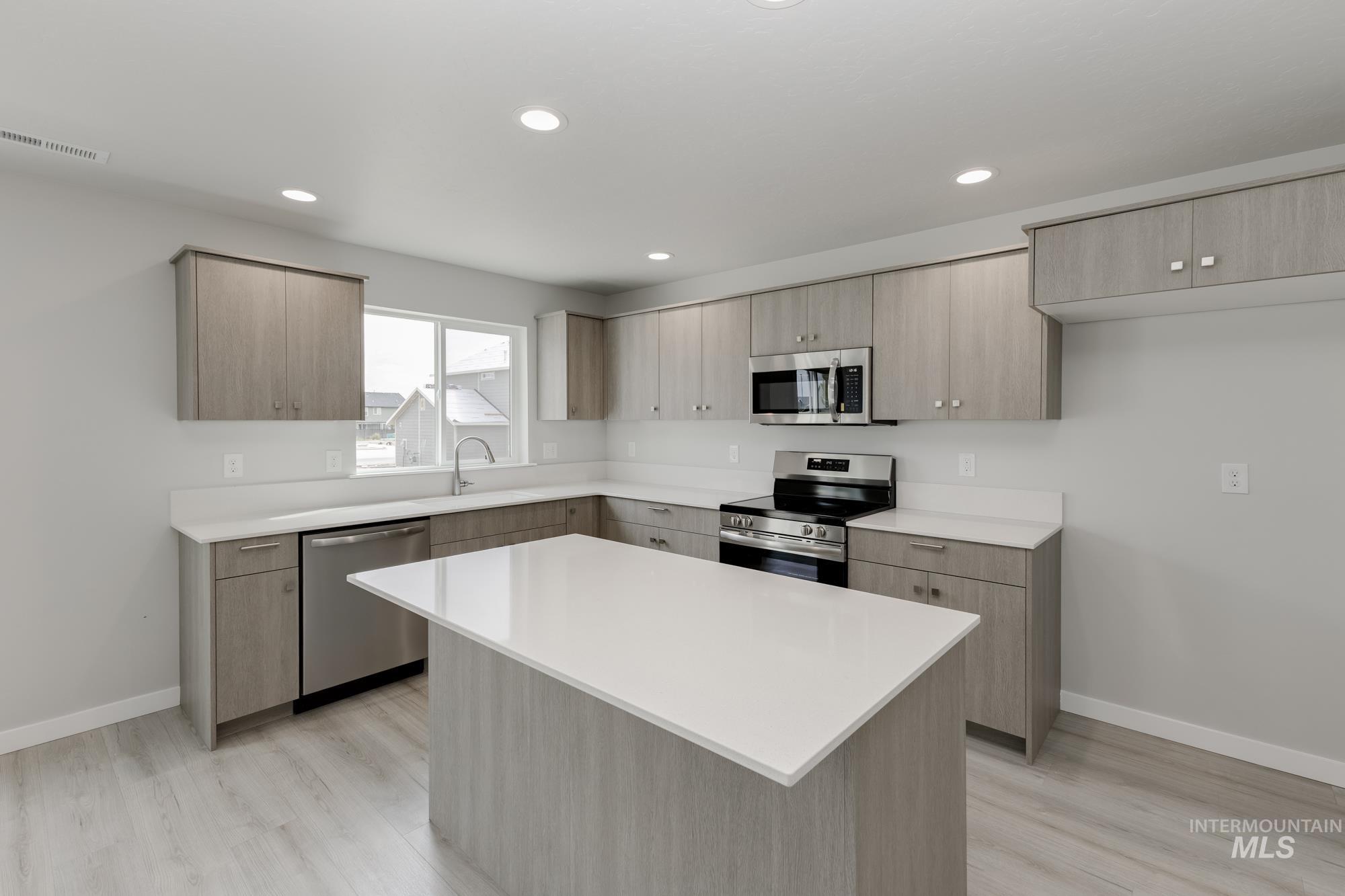 Kitchen featuring stainless steel appliances, modern cabinets, light brown cabinets, a center island, and light wood-style flooring