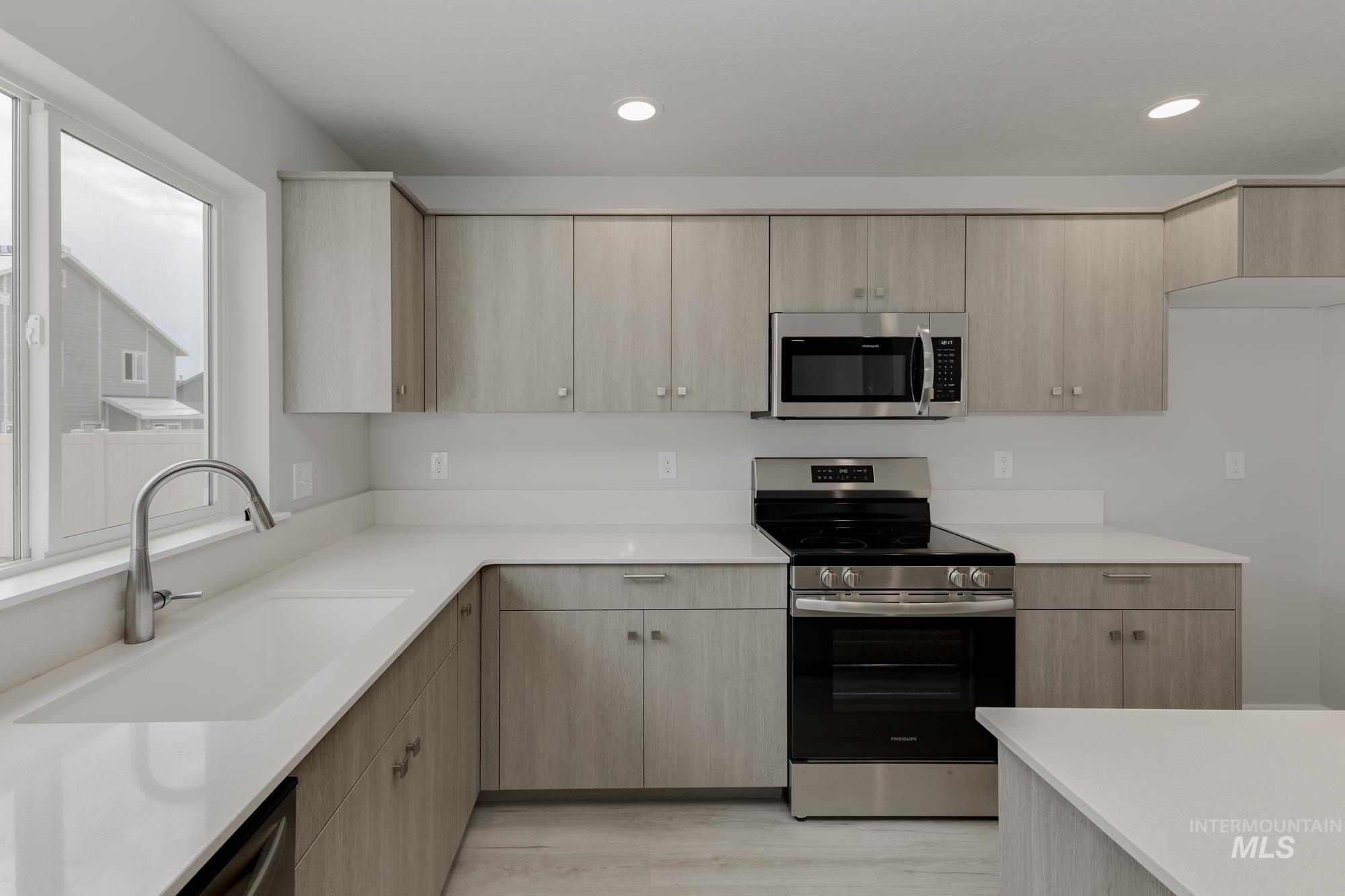 Kitchen featuring stainless steel appliances, light brown cabinets, light stone counters, modern cabinets, and recessed lighting
