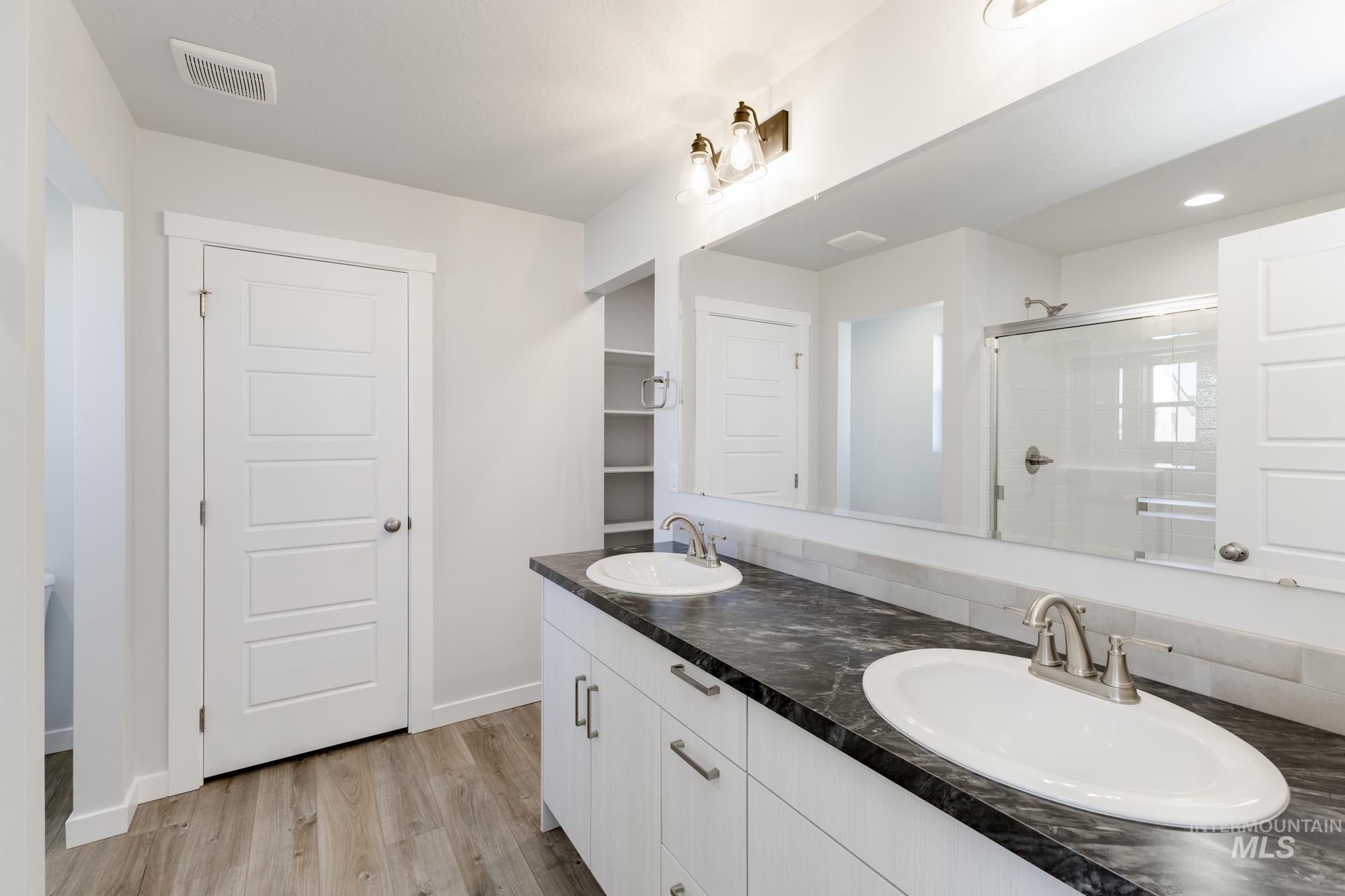 Bathroom featuring a stall shower, double vanity, wood finished floors, and a closet
