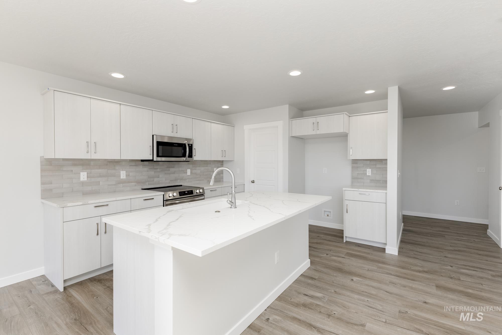 Kitchen with backsplash, light wood finished floors, white cabinets, stainless steel appliances, and recessed lighting