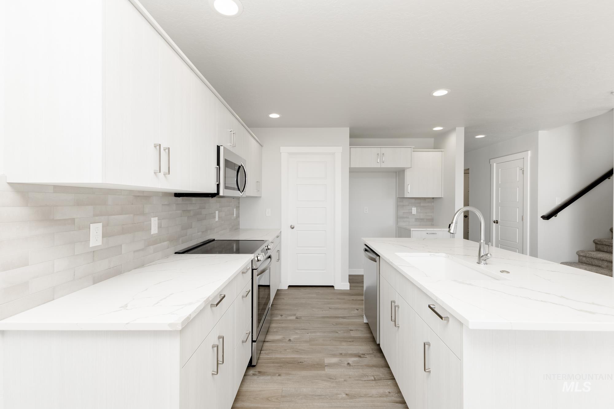 Kitchen with stainless steel appliances, light wood-style floors, recessed lighting, white cabinets, and backsplash