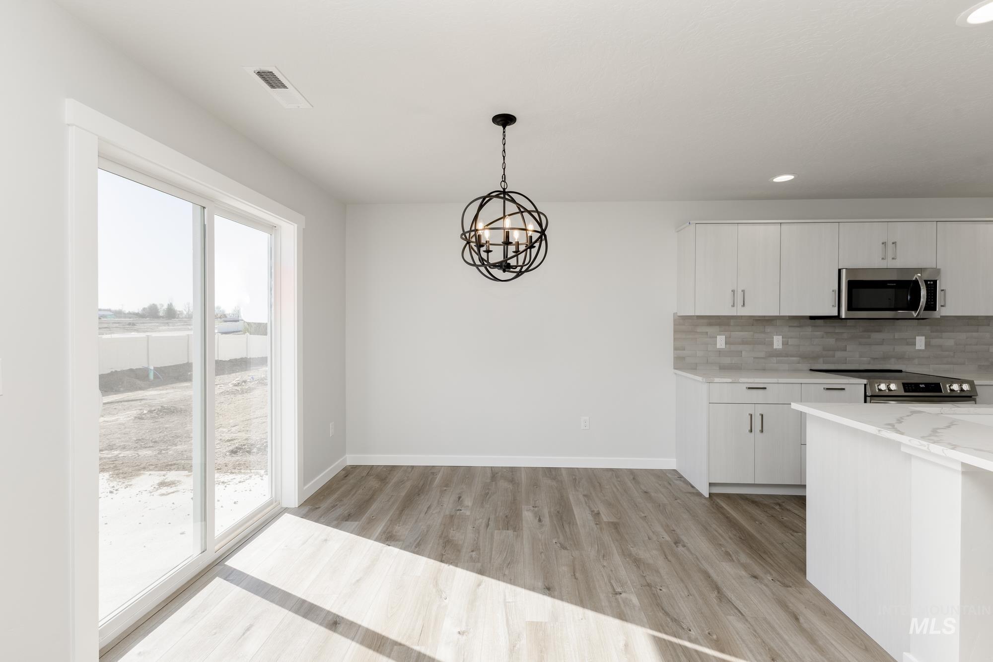 Kitchen with stainless steel appliances, light wood-style flooring, a chandelier, tasteful backsplash, and white cabinetry