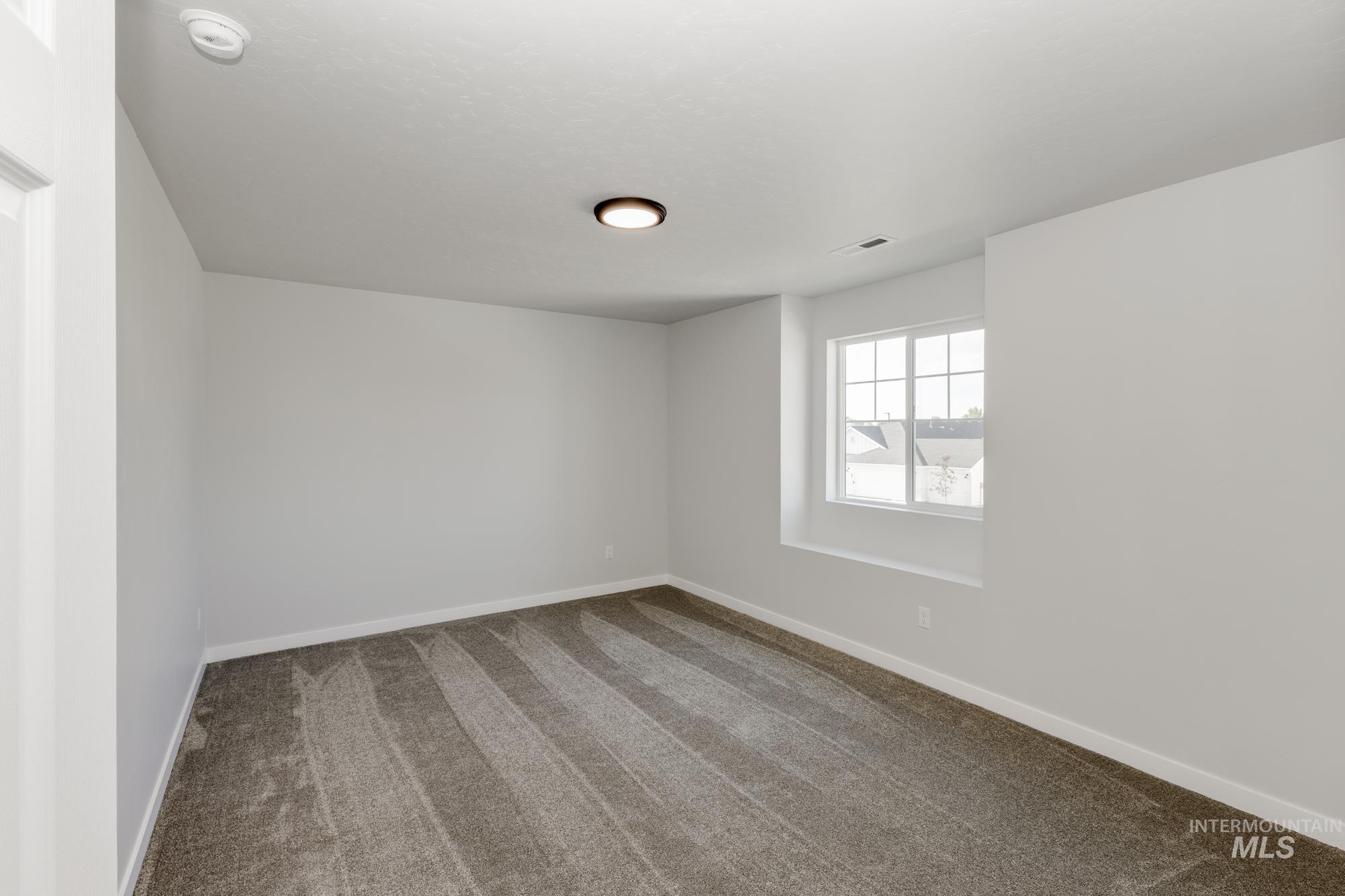 Unfurnished room with dark colored carpet and a smoke detector