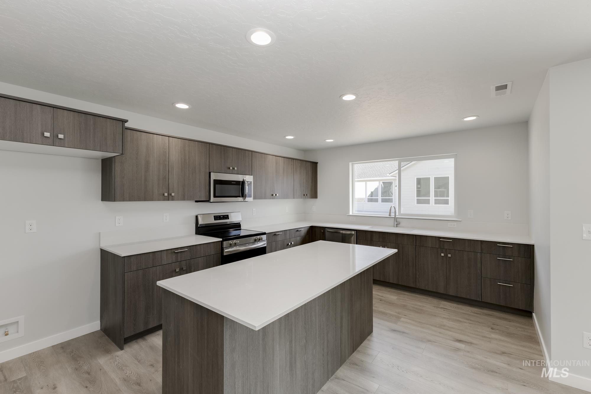 Kitchen featuring stainless steel appliances, a kitchen island, light countertops, light wood finished floors, and dark brown cabinets