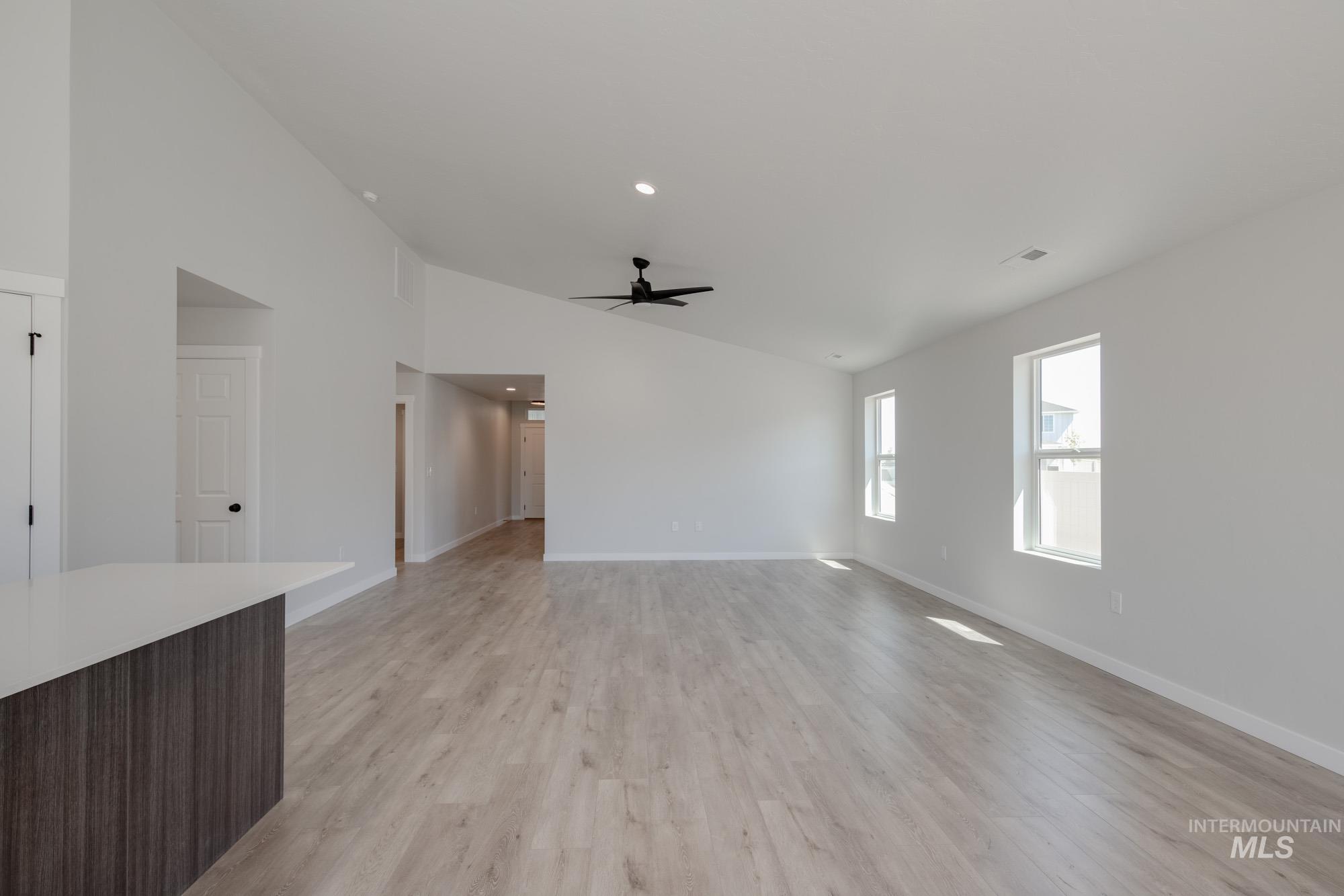 Unfurnished living room with light wood-style flooring, a ceiling fan, high vaulted ceiling, and recessed lighting