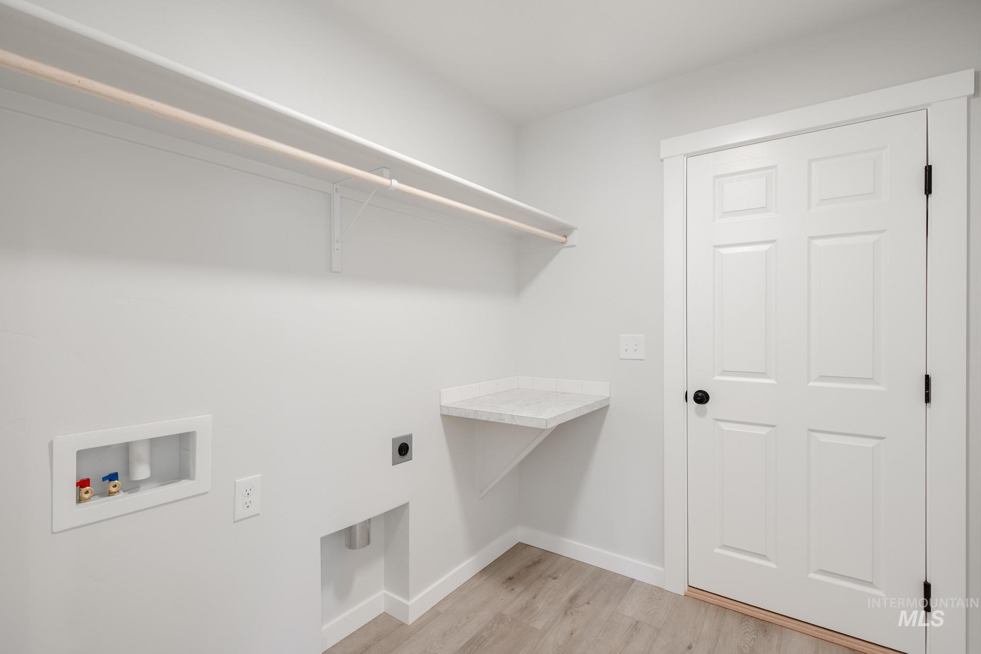 Washroom with hookup for a washing machine, electric dryer hookup, and light wood-style flooring