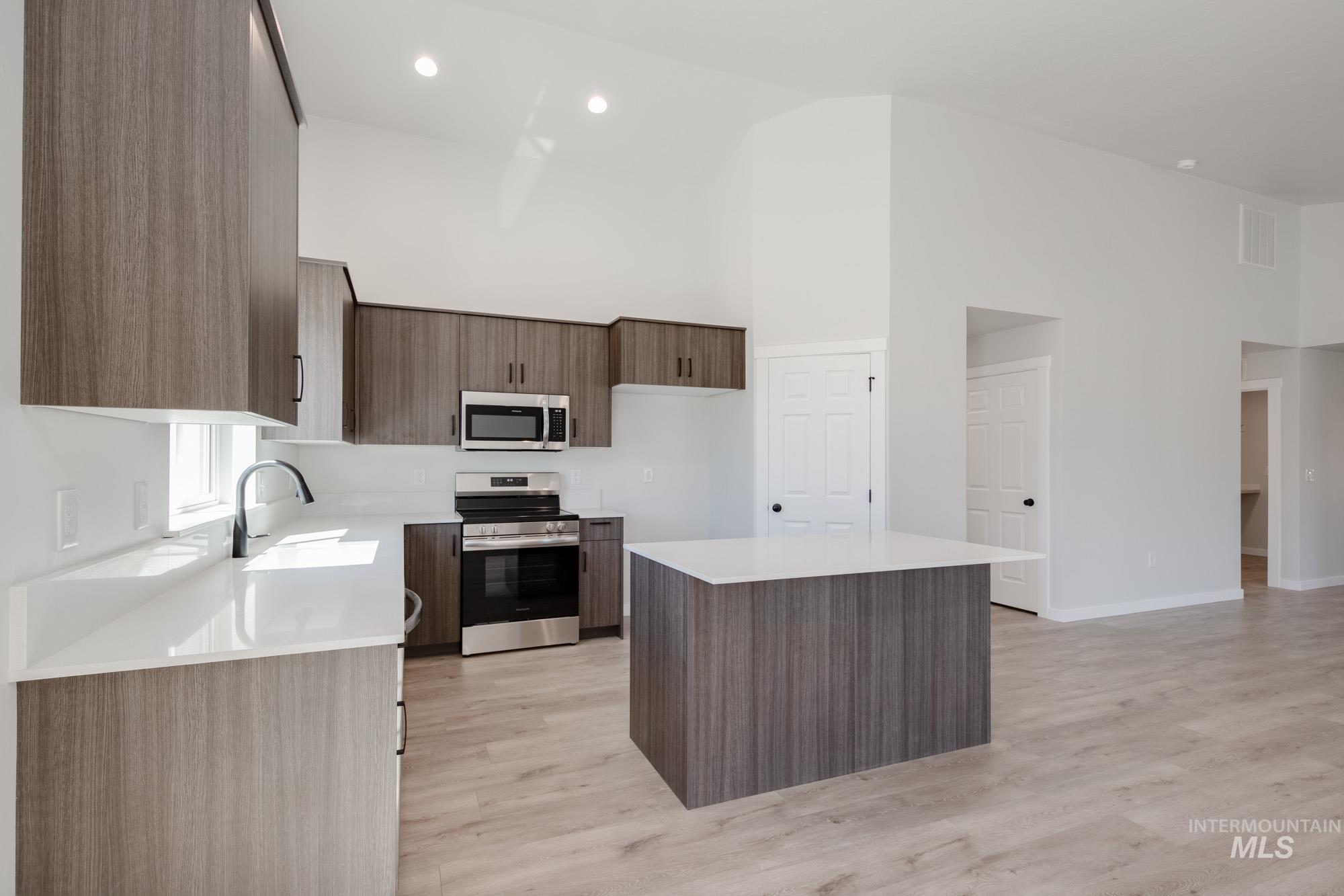 Kitchen featuring stainless steel appliances, high vaulted ceiling, light wood-type flooring, light countertops, and a center island