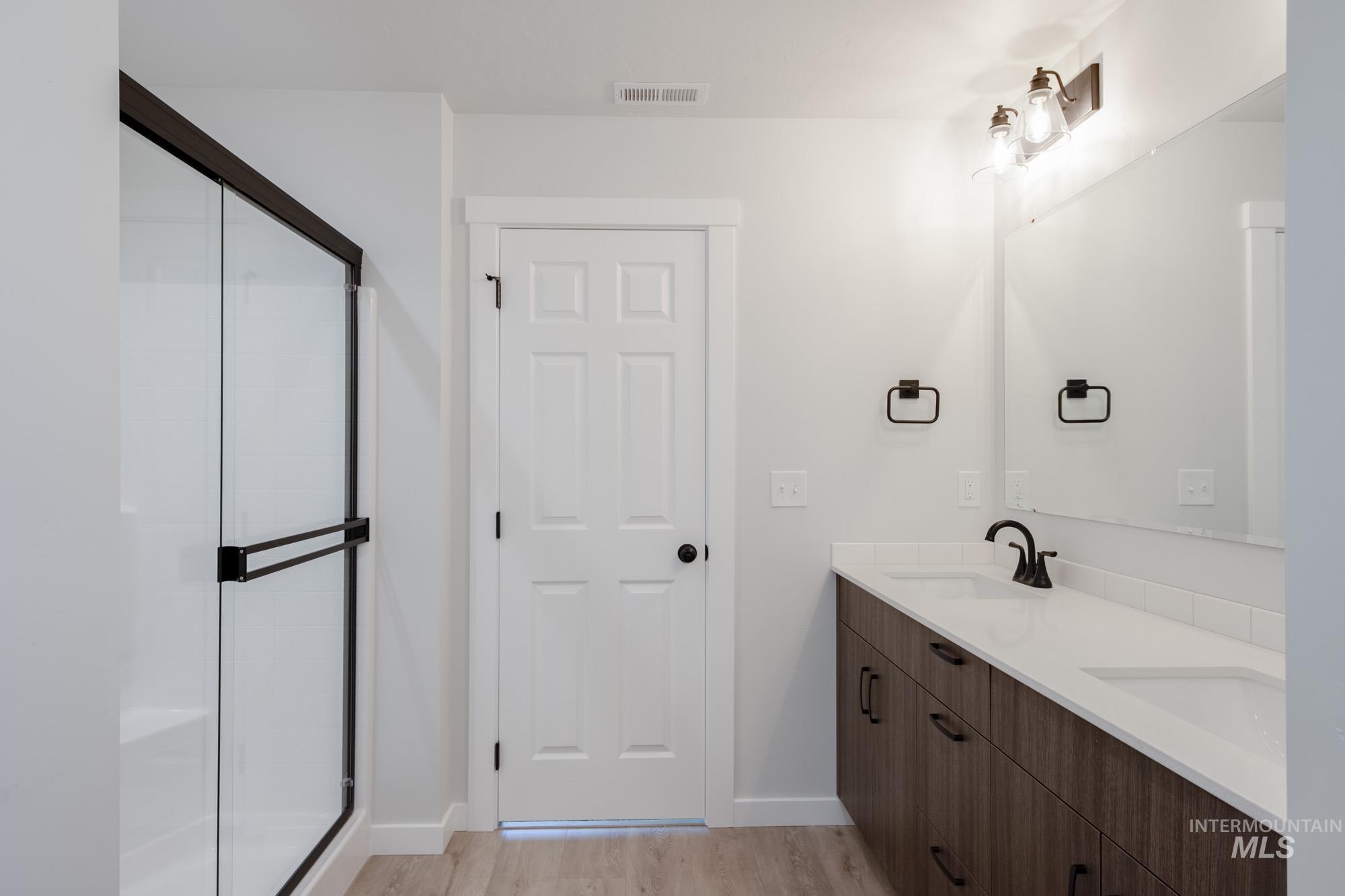 Full bathroom with double vanity, wood finished floors, and a stall shower