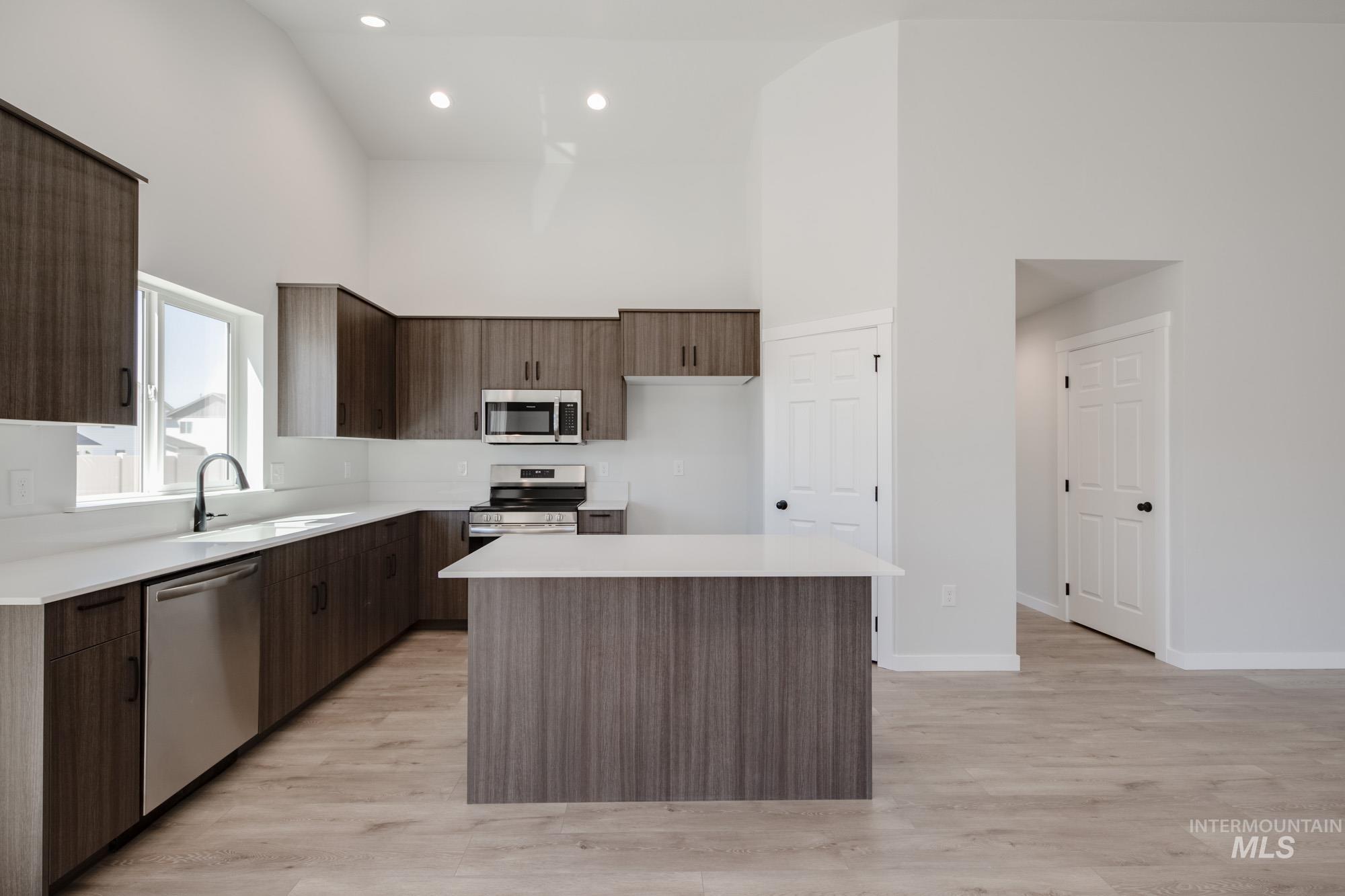 Kitchen featuring light wood finished floors, a kitchen island, a high ceiling, stainless steel appliances, and light countertops