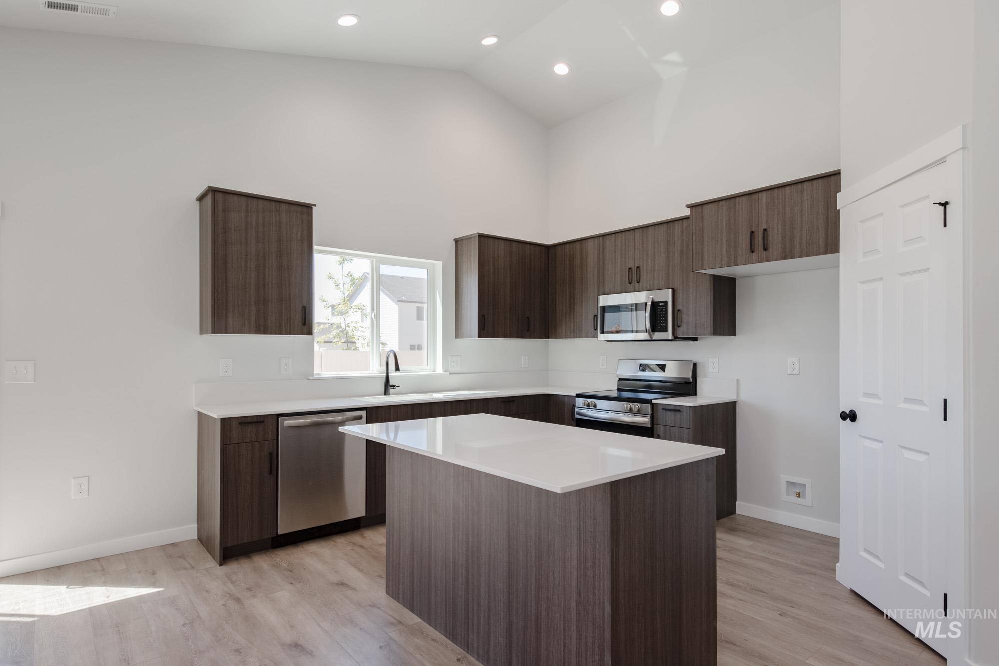 Kitchen with stainless steel appliances, high vaulted ceiling, light wood-style flooring, light countertops, and dark brown cabinetry