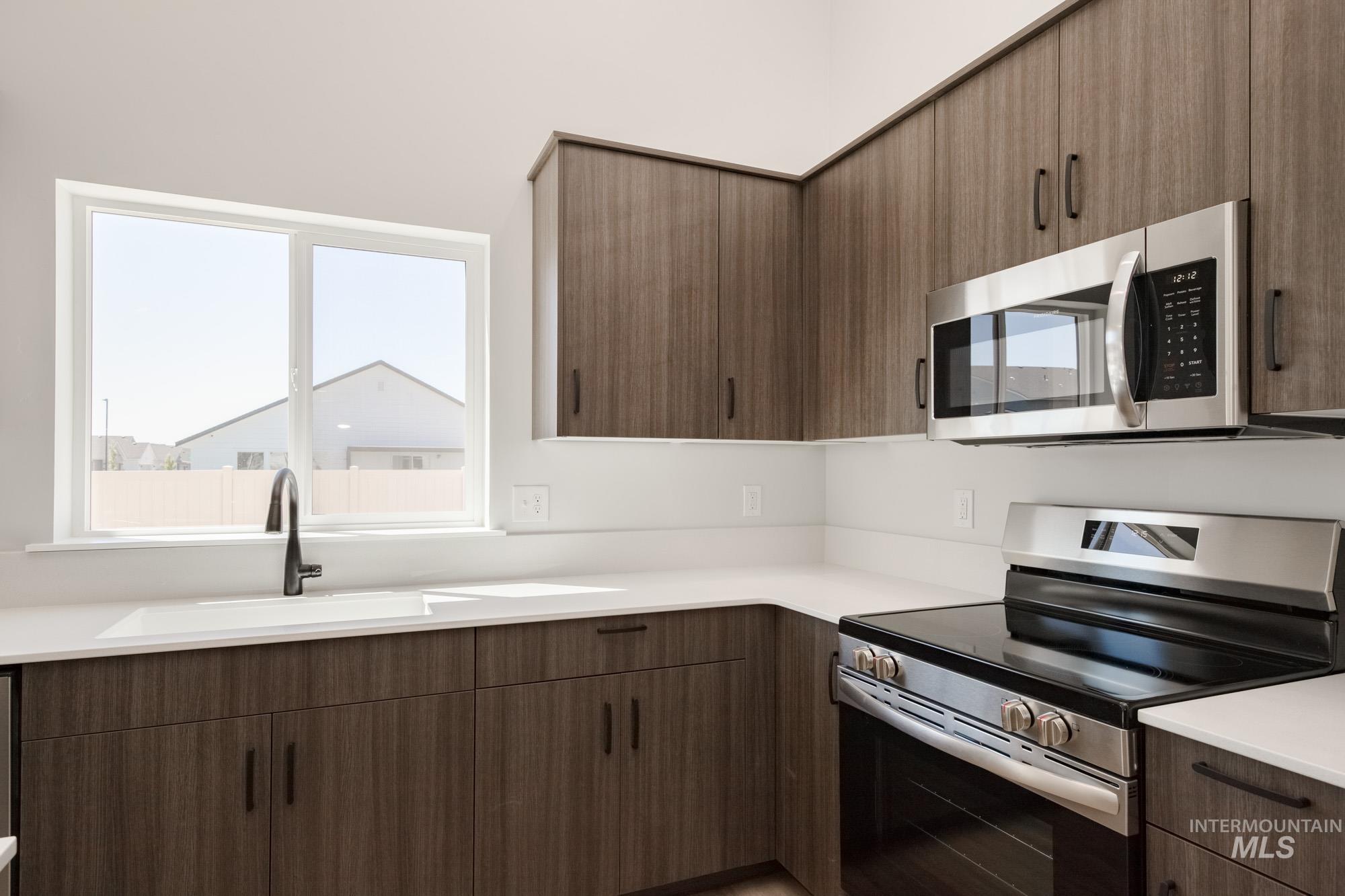 Kitchen featuring stainless steel appliances, light countertops, dark brown cabinetry, and modern cabinets