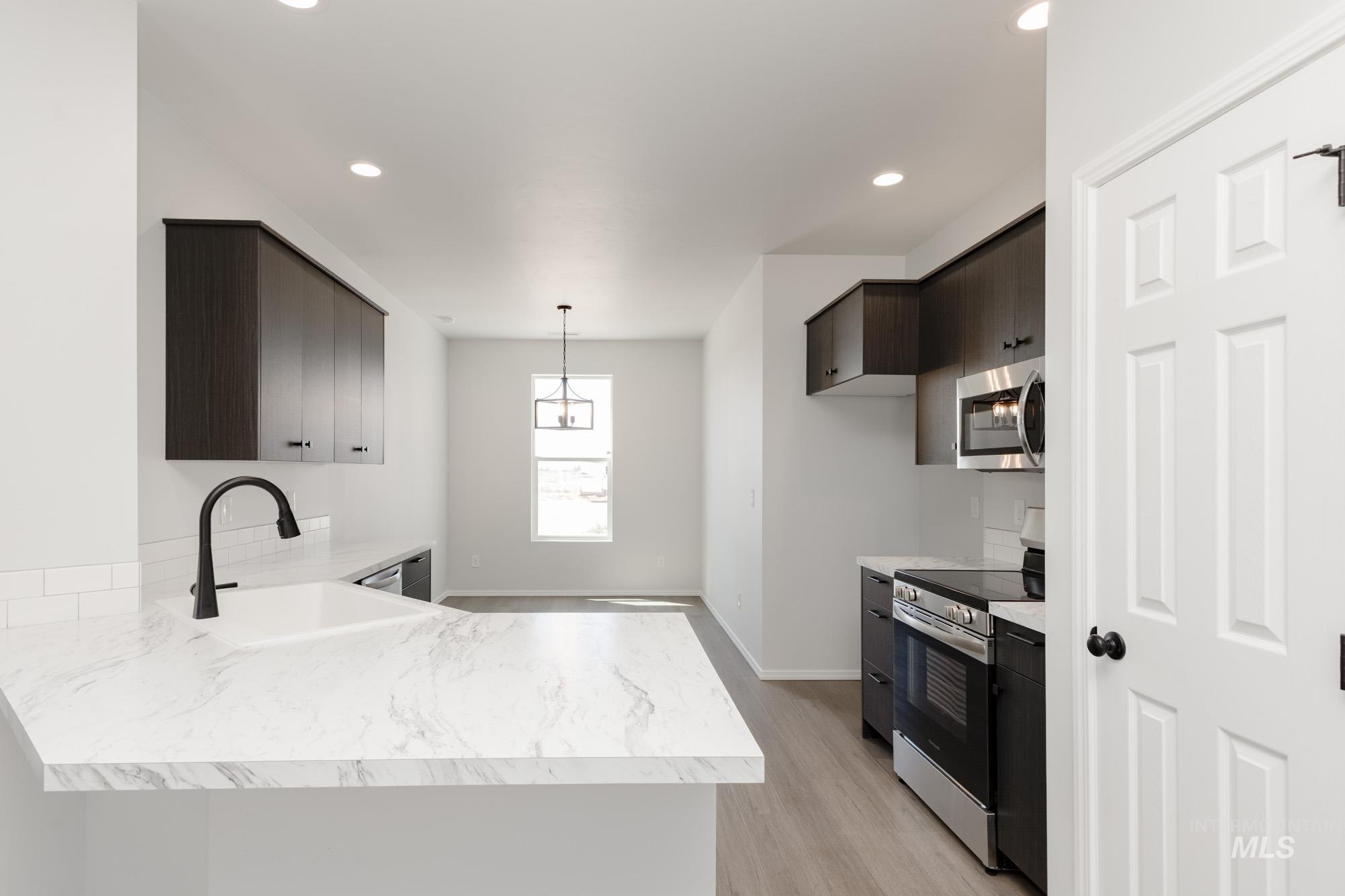 Kitchen featuring stainless steel appliances, dark brown cabinets, a peninsula, light wood-style floors, and hanging light fixtures