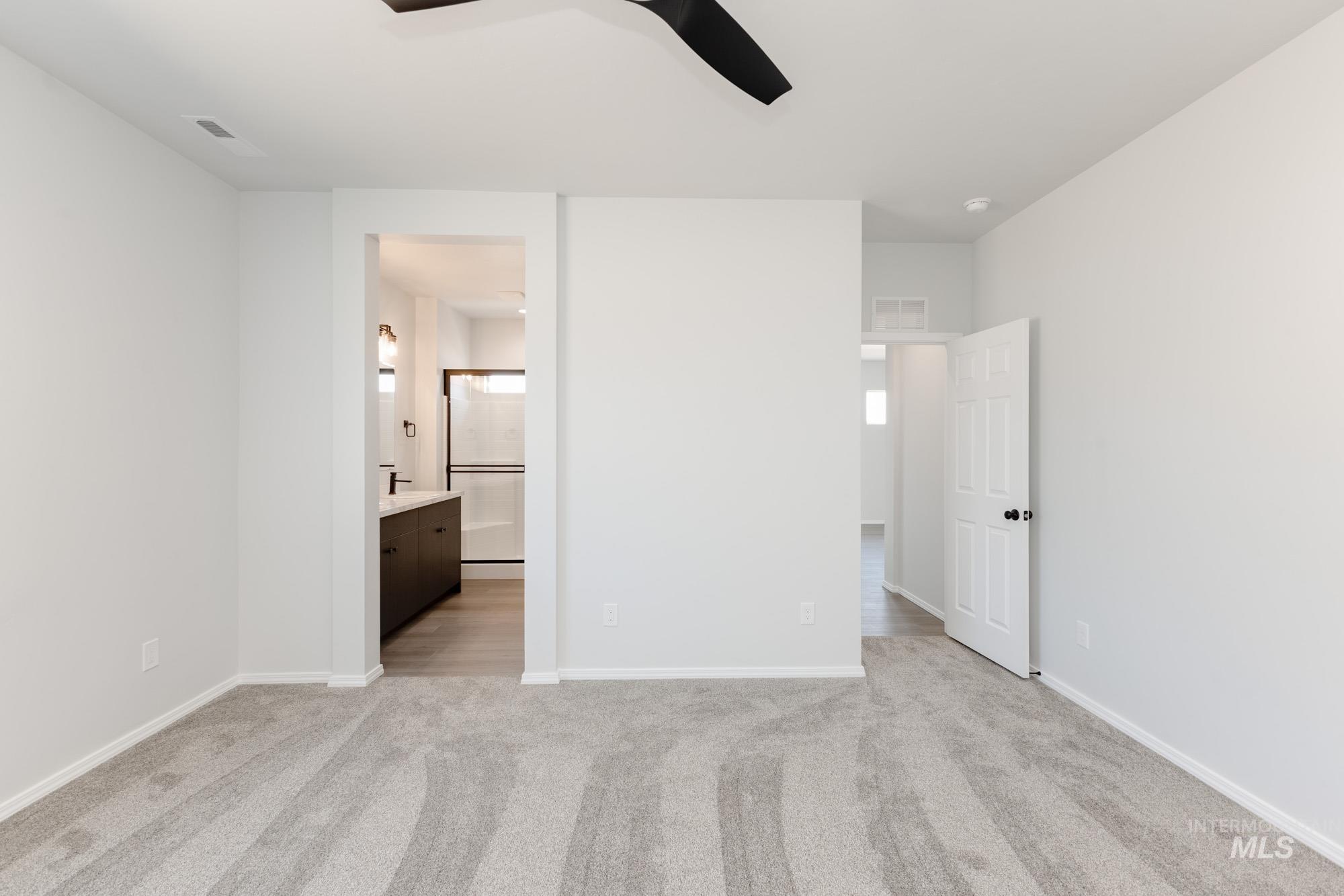 Unfurnished bedroom with light carpet, ceiling fan, and ensuite bath