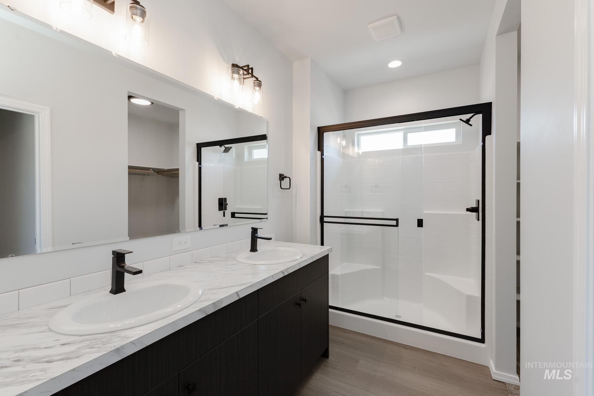Full bath featuring a shower stall, a spacious closet, double vanity, light wood finished floors, and recessed lighting