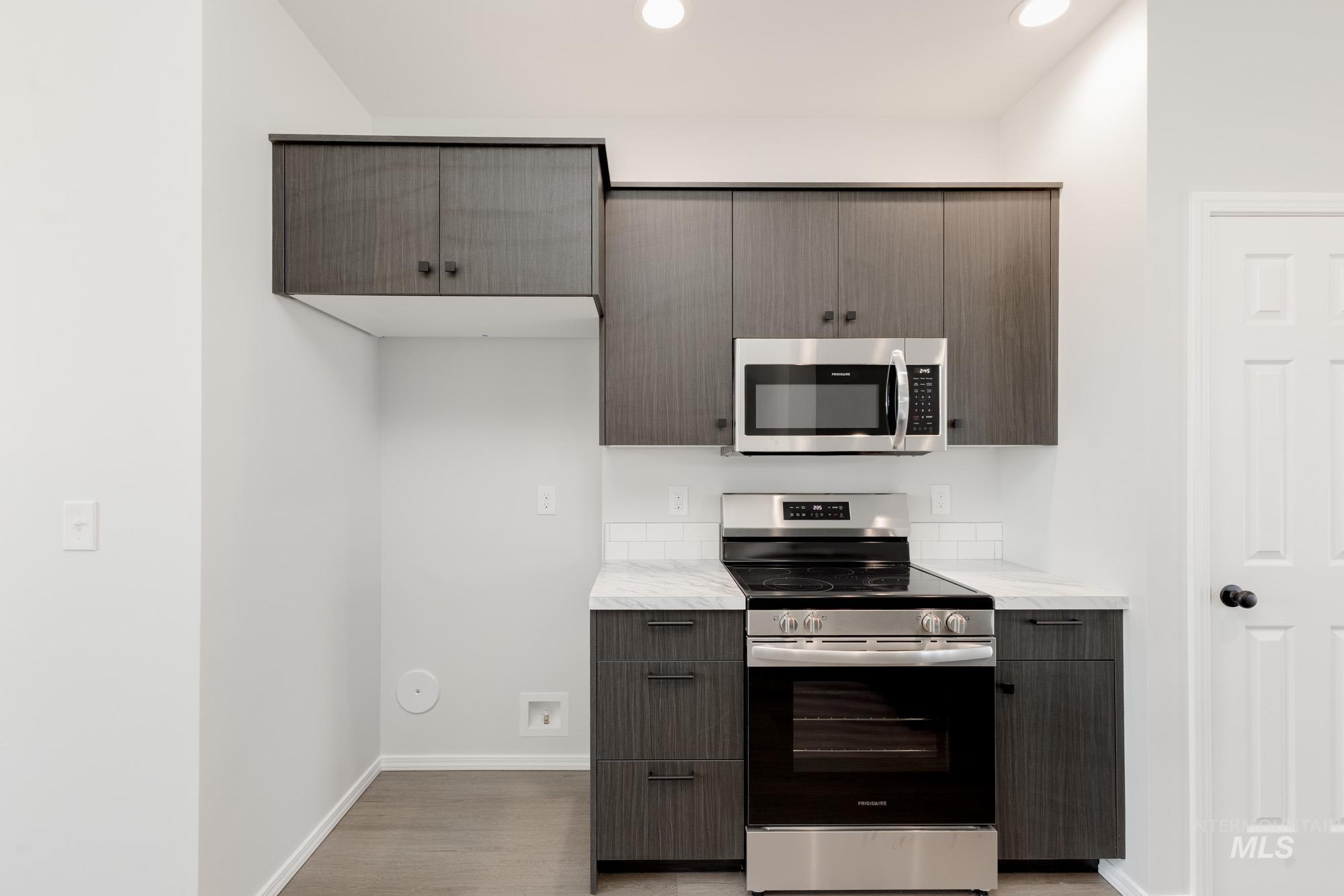 Kitchen with appliances with stainless steel finishes, modern cabinets, light wood-style flooring, light stone counters, and dark brown cabinets