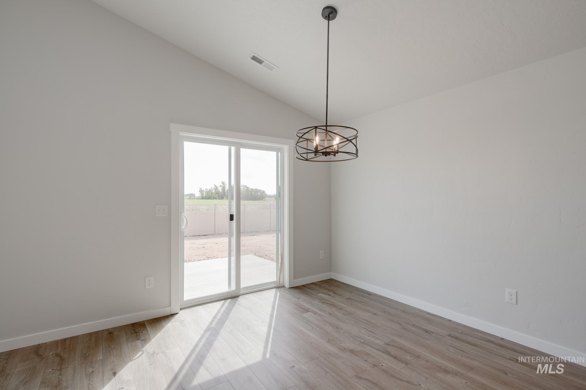 Empty room featuring lofted ceiling, a chandelier, and light wood-style flooring