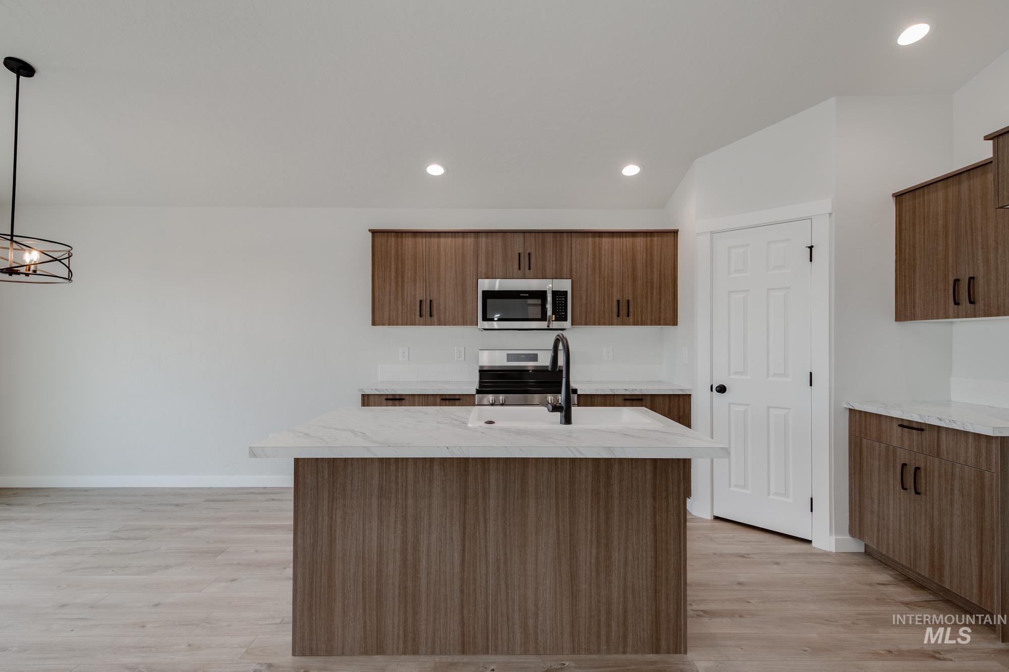 Kitchen with a kitchen island with sink, appliances with stainless steel finishes, recessed lighting, light wood-style flooring, and decorative light fixtures