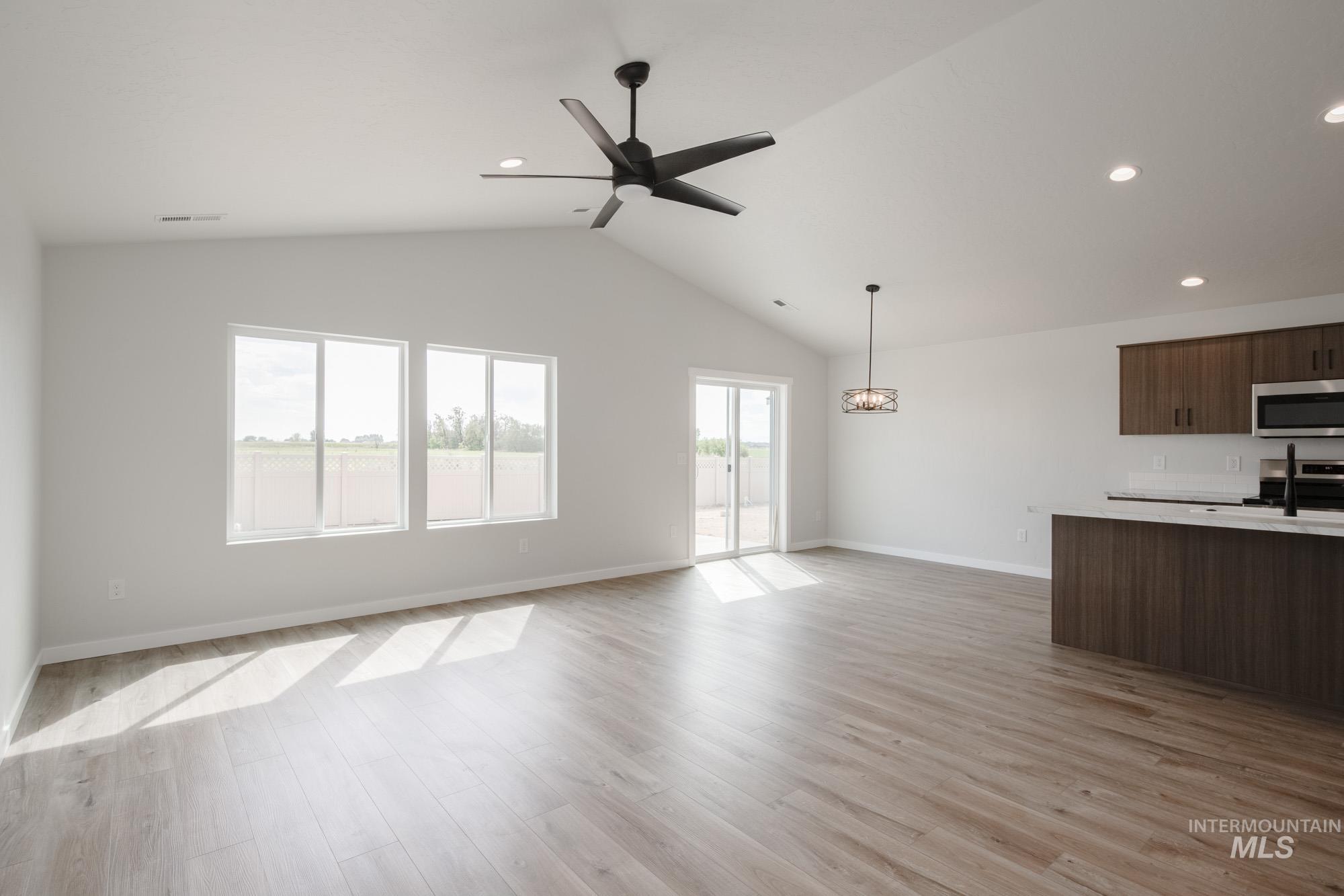 Unfurnished living room with vaulted ceiling, light wood-style floors, a ceiling fan, recessed lighting, and a chandelier