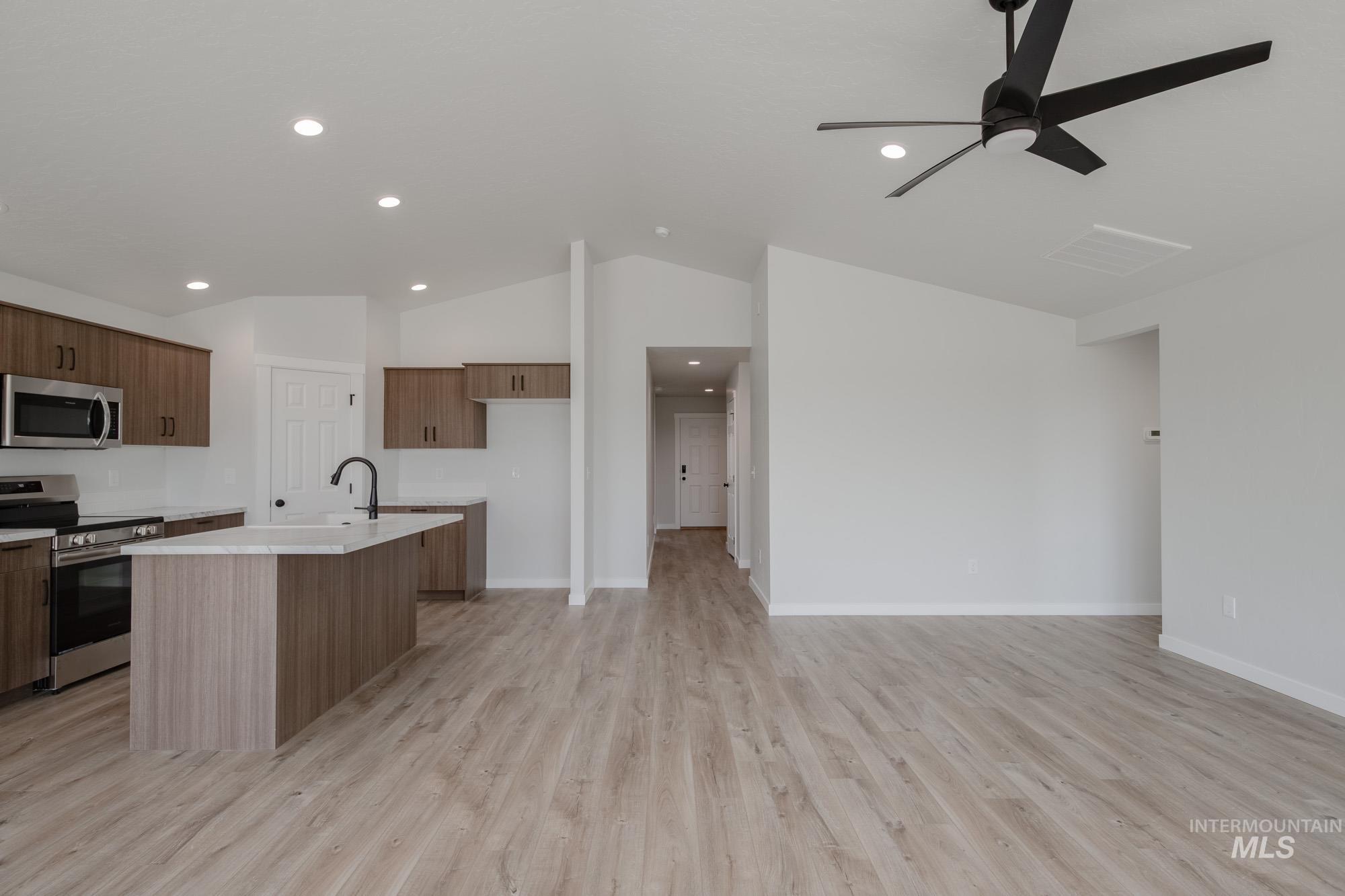 Kitchen featuring appliances with stainless steel finishes, a kitchen island with sink, vaulted ceiling, light wood-style flooring, and open floor plan