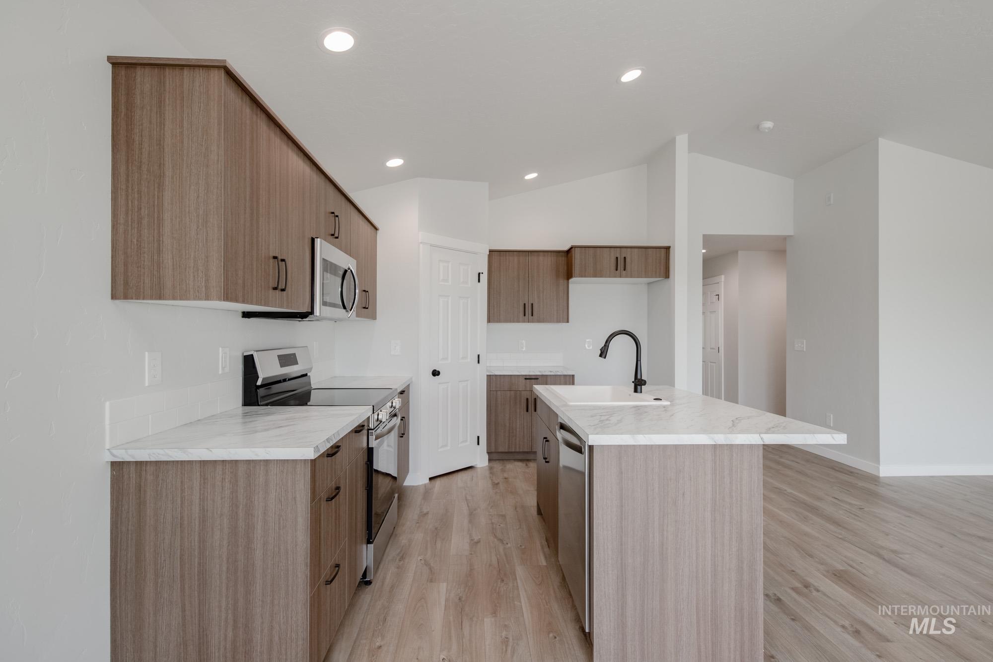 Kitchen with stainless steel appliances, light wood-type flooring, an island with sink, vaulted ceiling, and modern cabinets