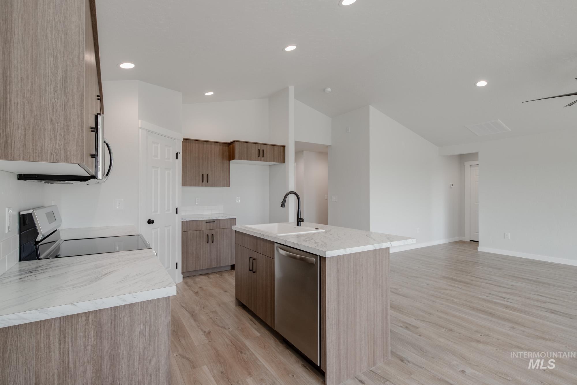 Kitchen featuring a center island with sink, light wood-type flooring, stainless steel appliances, recessed lighting, and lofted ceiling