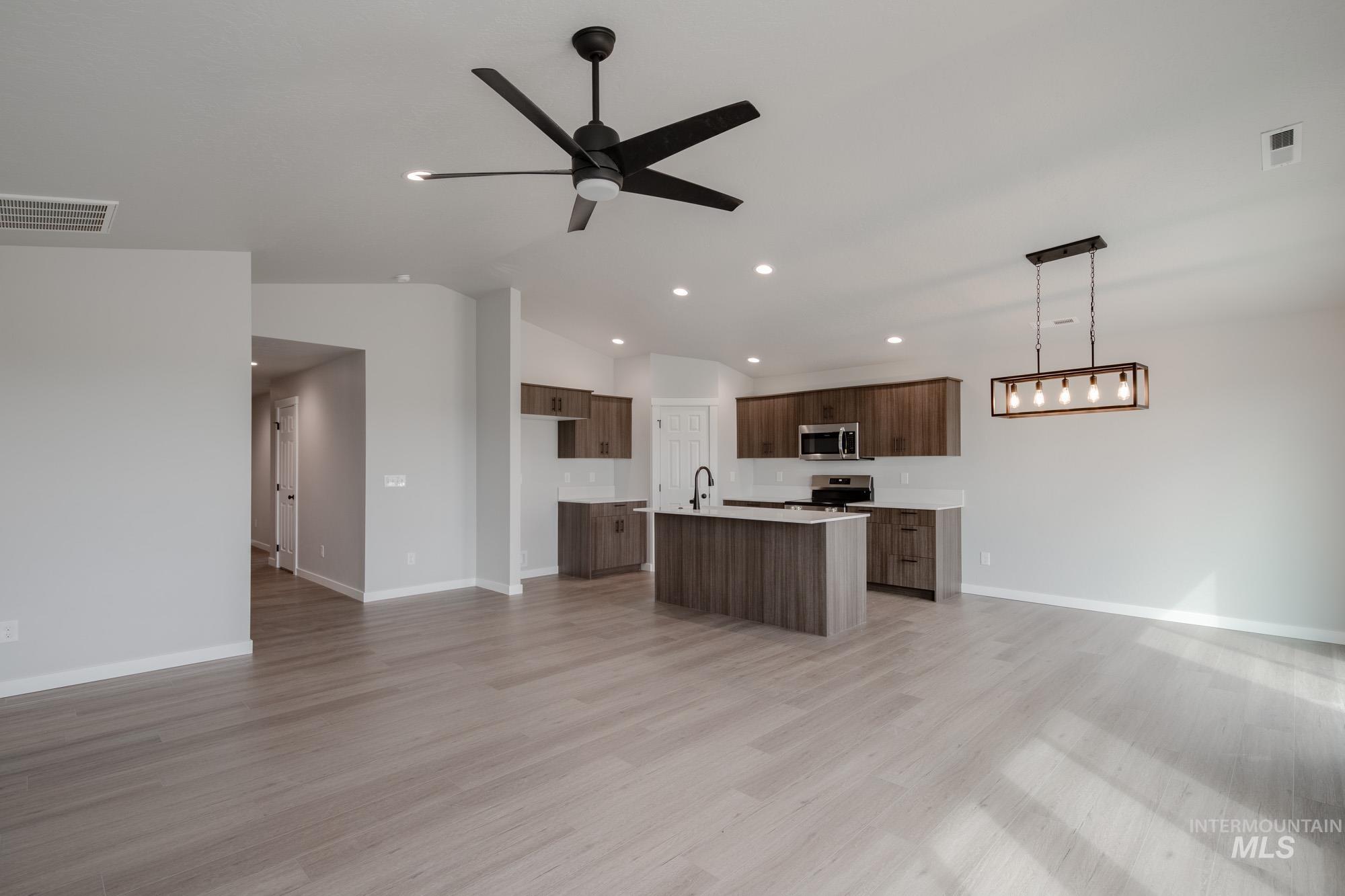 Kitchen featuring open floor plan, light countertops, a kitchen island with sink, lofted ceiling, and light wood-style floors