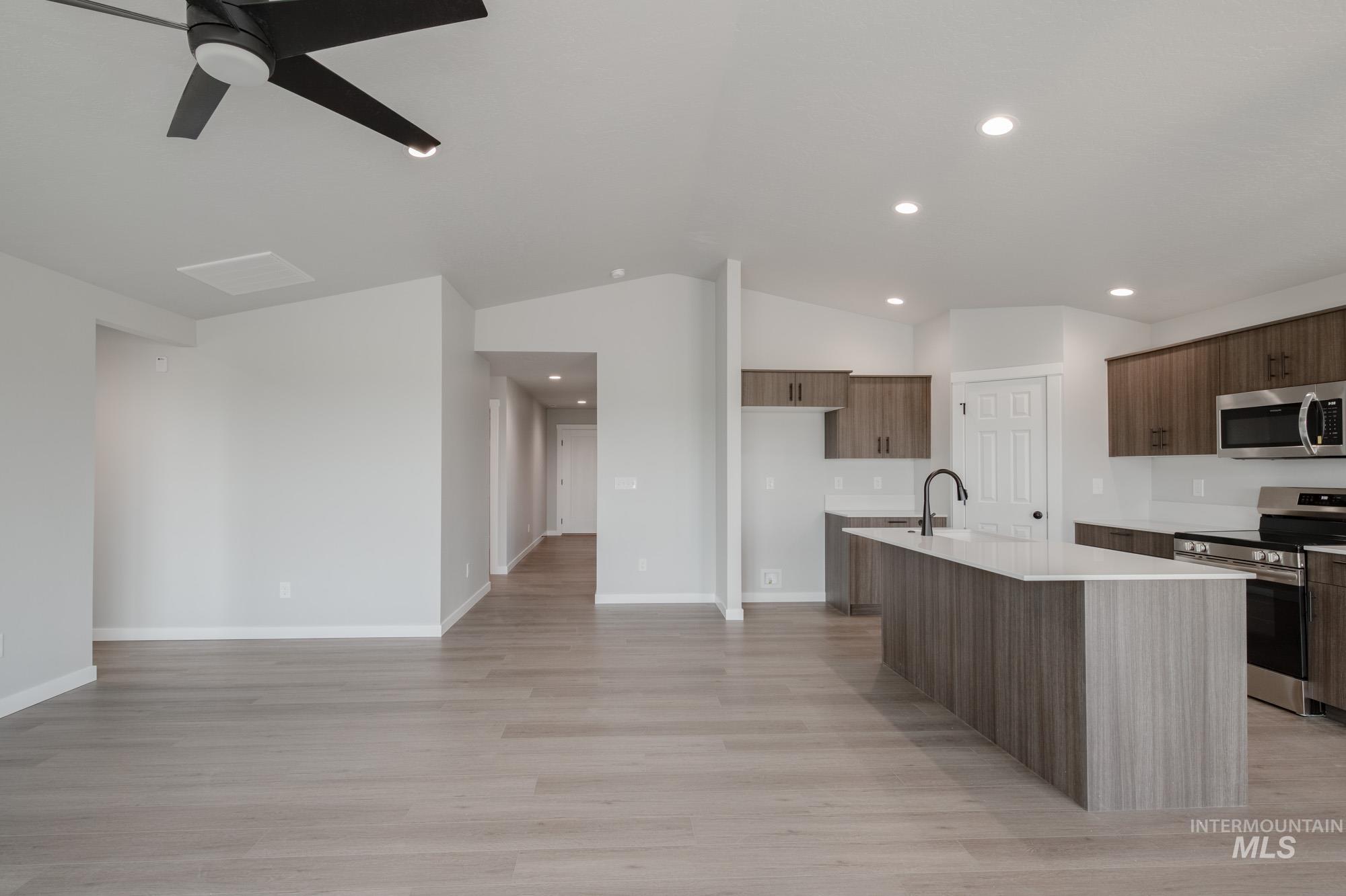 Kitchen featuring stainless steel appliances, vaulted ceiling, a center island with sink, light wood-style floors, and modern cabinets