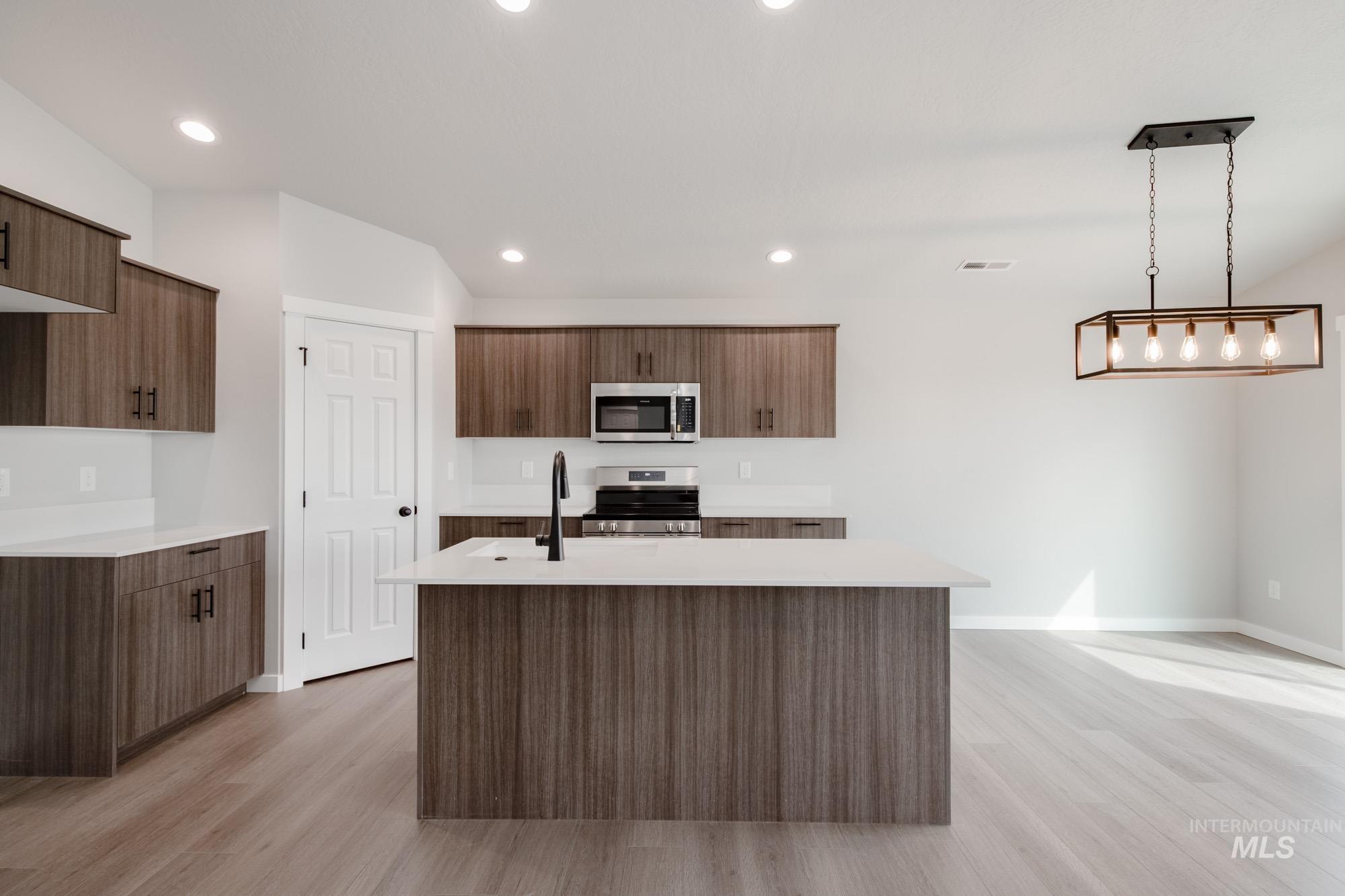 Kitchen with appliances with stainless steel finishes, light wood-style flooring, recessed lighting, a kitchen island with sink, and pendant lighting