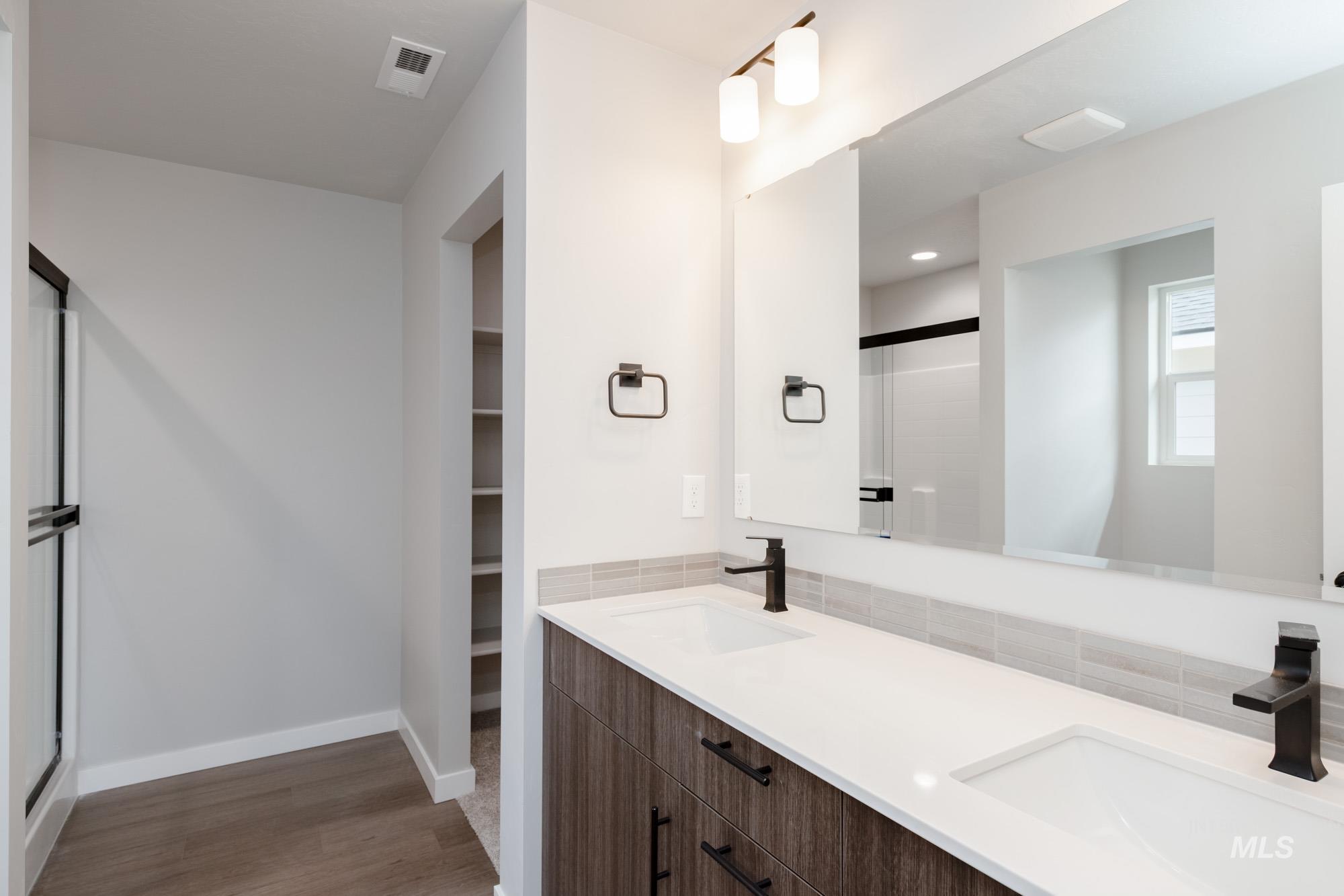 Full bath with double vanity, a shower stall, dark wood-style flooring, and a walk in closet
