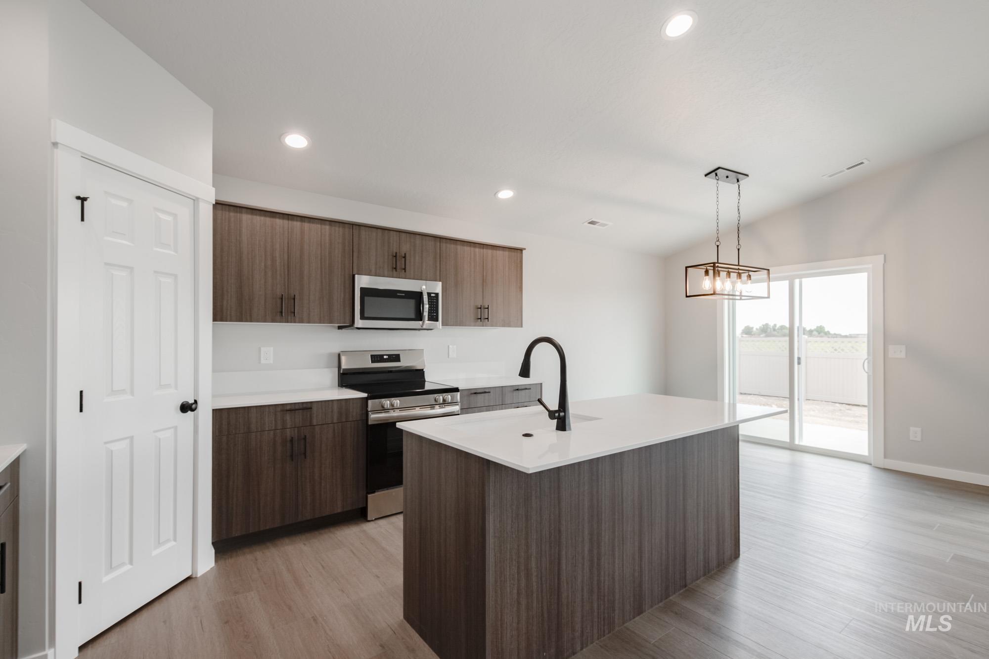 Kitchen with stainless steel appliances, light wood-style flooring, pendant lighting, a center island with sink, and recessed lighting