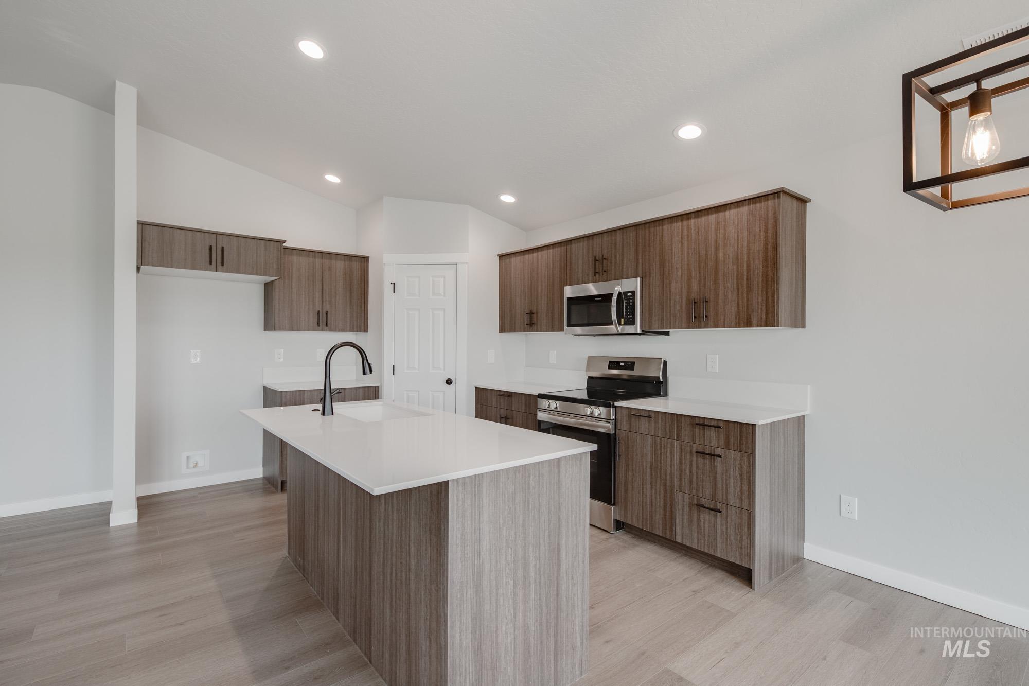 Kitchen with stainless steel appliances, vaulted ceiling, a center island with sink, modern cabinets, and light wood-style flooring