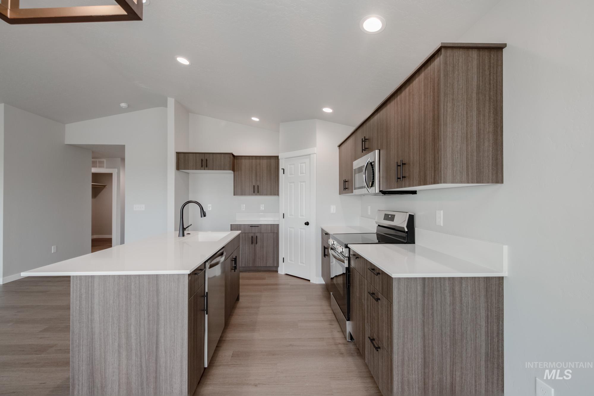 Kitchen featuring appliances with stainless steel finishes, modern cabinets, a center island with sink, light stone countertops, and light wood finished floors