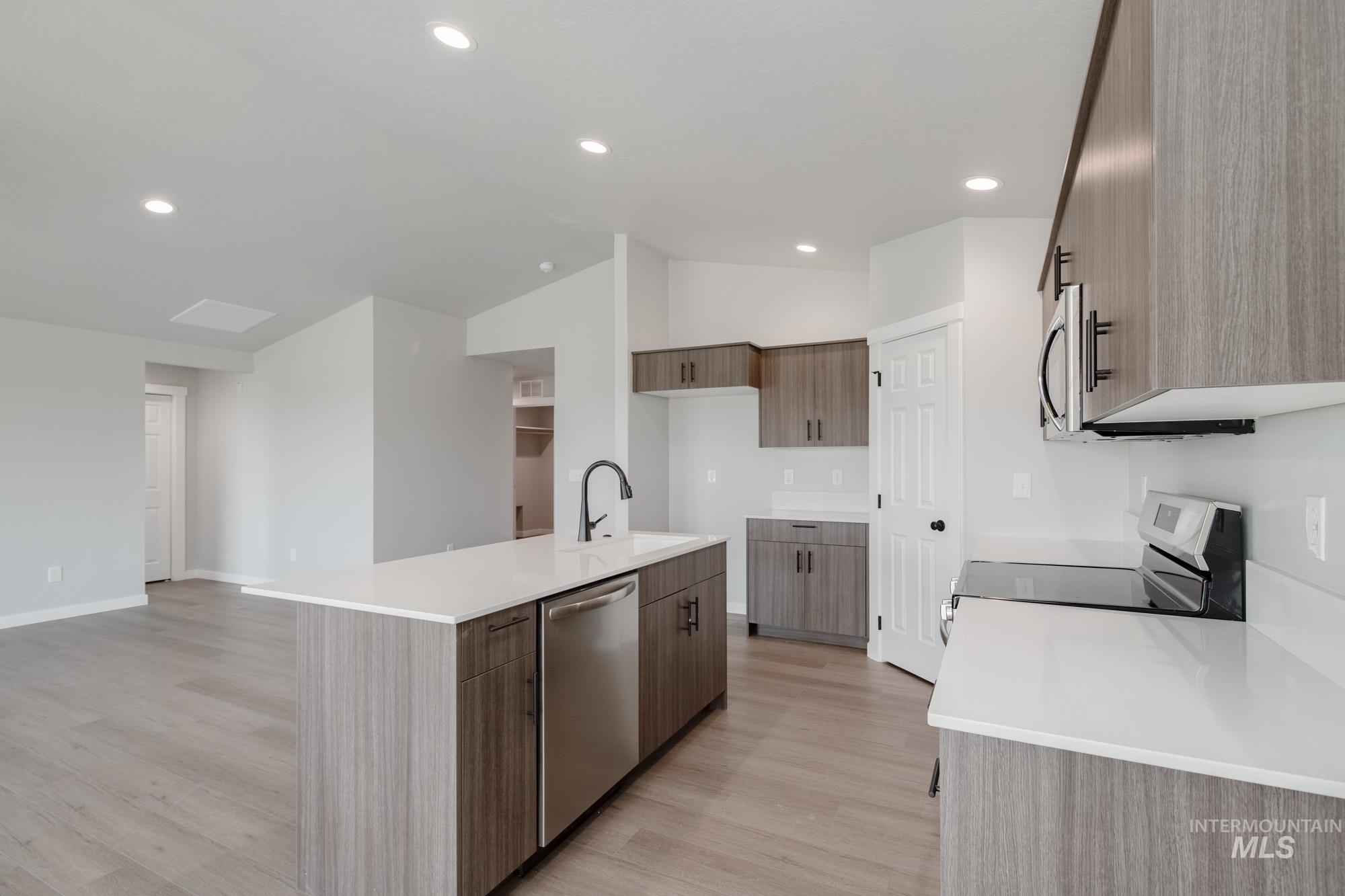 Kitchen with appliances with stainless steel finishes, light wood-style flooring, lofted ceiling, recessed lighting, and light stone countertops