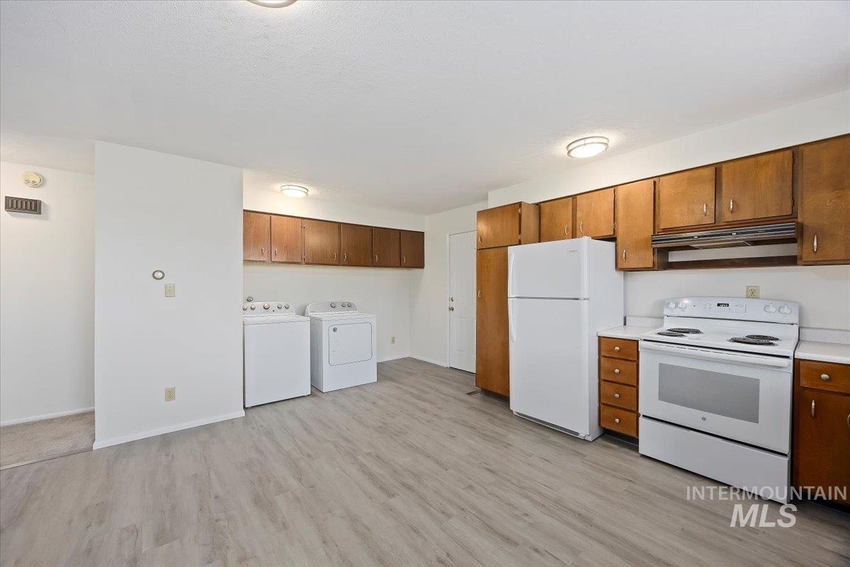 Kitchen featuring white appliances, light countertops, light wood finished floors, brown cabinetry, and under cabinet range hood