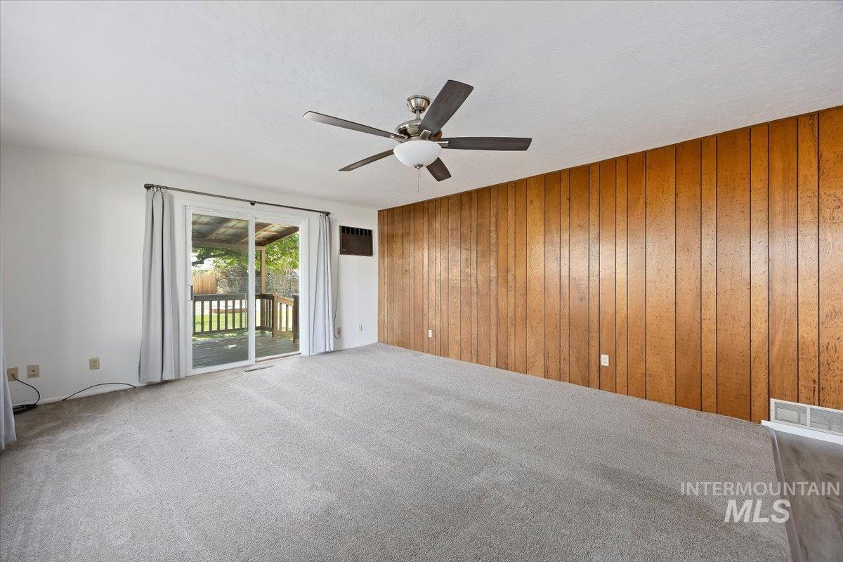 Unfurnished room featuring carpet flooring, wood walls, ceiling fan, and a textured ceiling