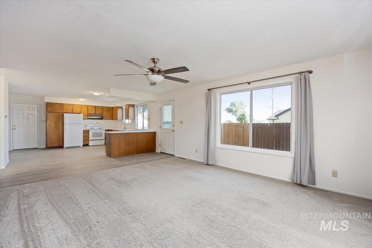 Unfurnished living room with healthy amount of natural light, ceiling fan, light colored carpet, and a textured ceiling