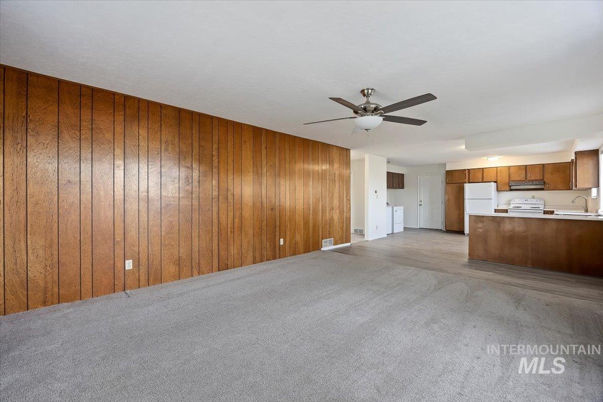 Unfurnished living room with ceiling fan, wooden walls, light colored carpet, and separate washer and dryer